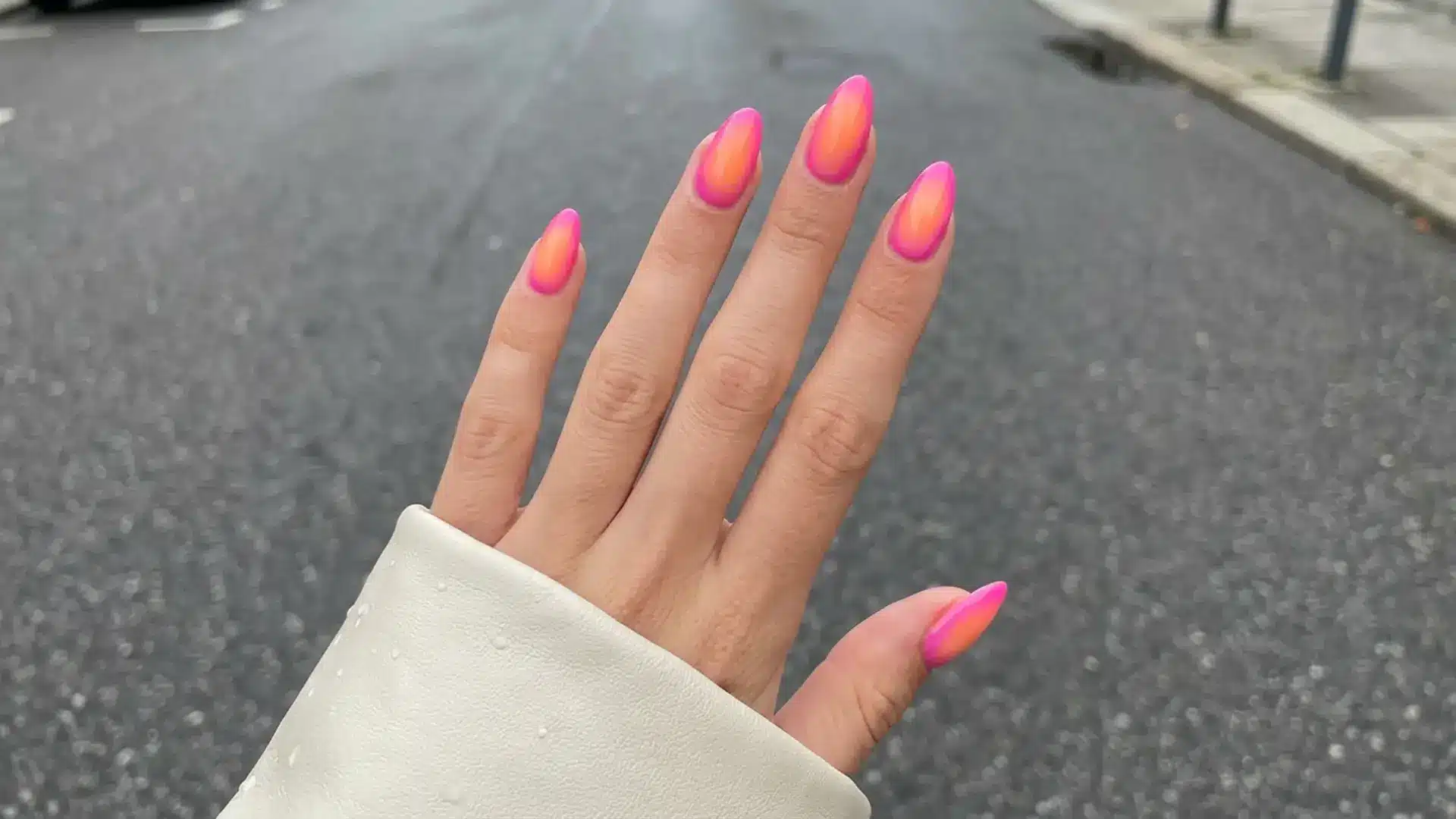 Bright neon pink and orange aura nail design on almond nails photographed outdoors showing bold spring break nails idea
