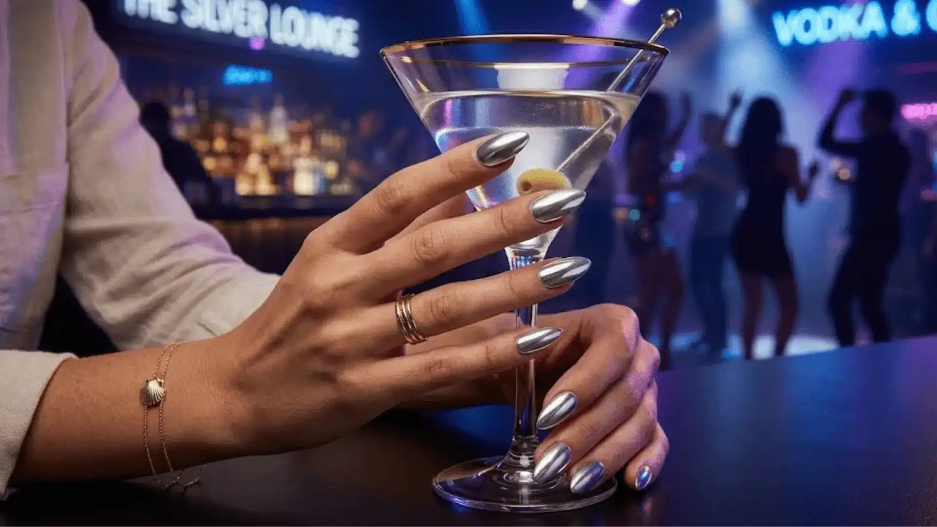 Chrome silver manicure holding martini glass in nightclub with colorful lights
