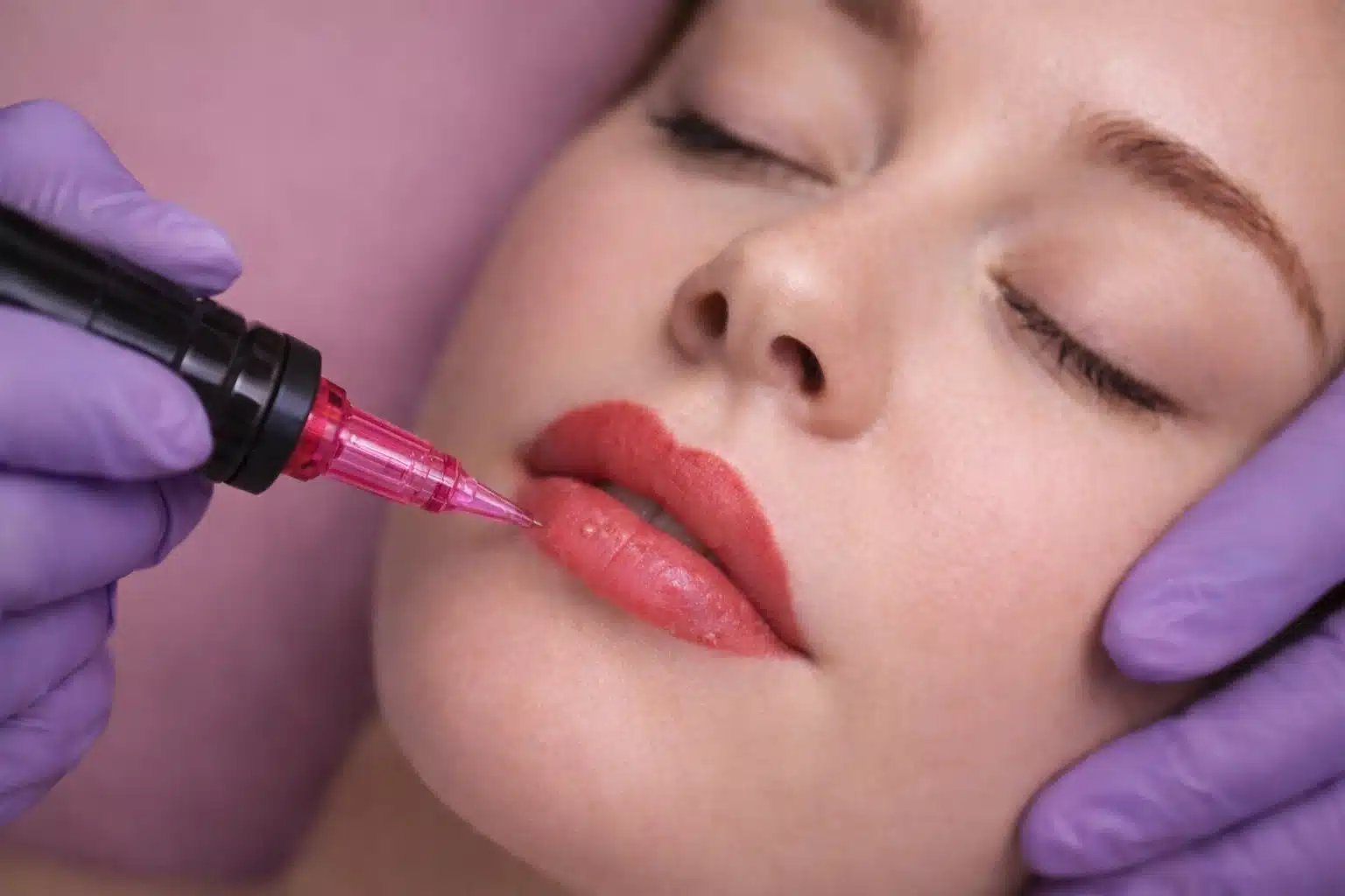 Close up of lip blush procedure with cosmetic tattoo device applying pigment to lips during professional treatment