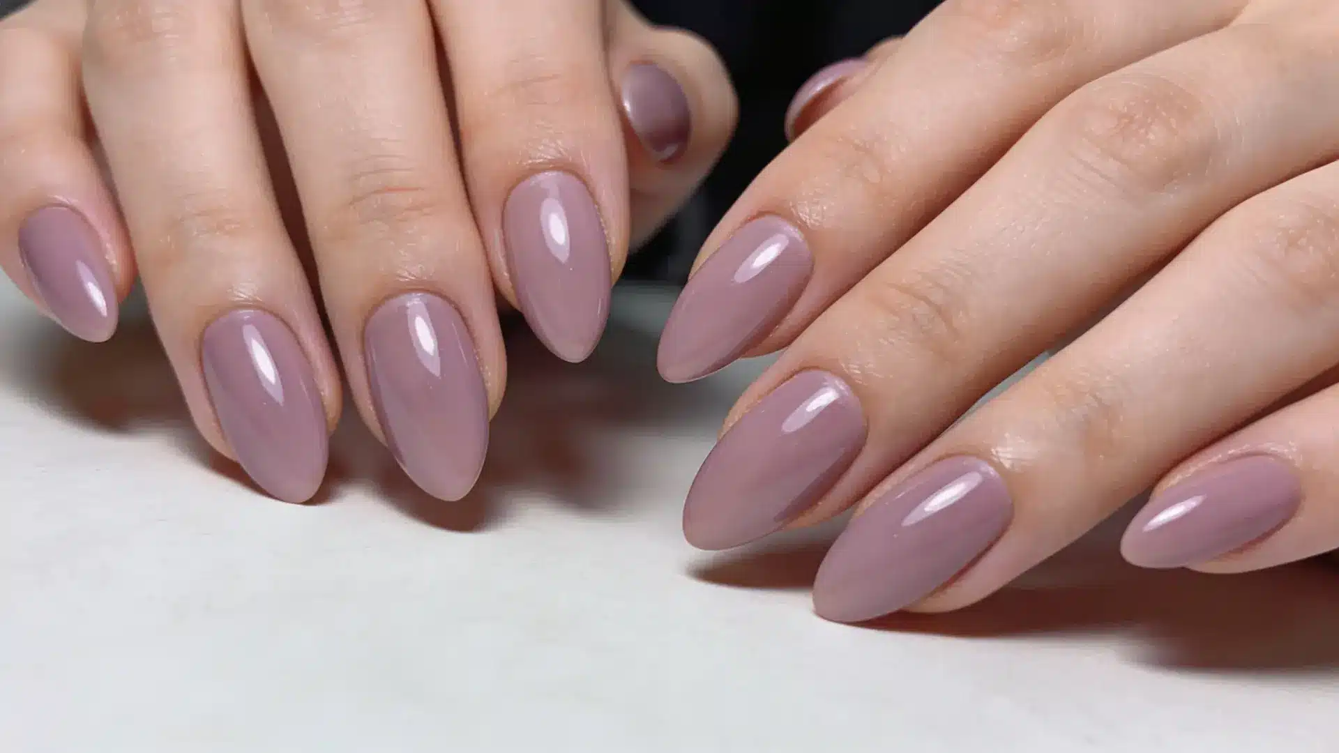Glossy mauve almond shaped manicure on hands resting on table with smooth polished finish