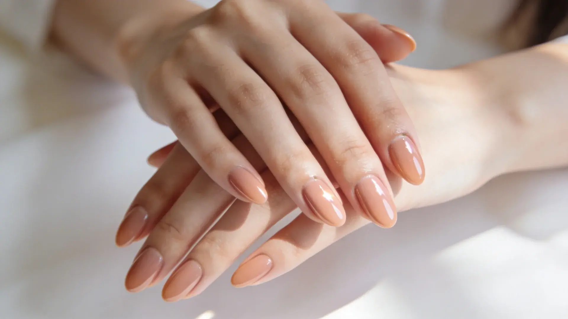 Glossy nude manicure with almond shaped nails in soft natural lighting close up
