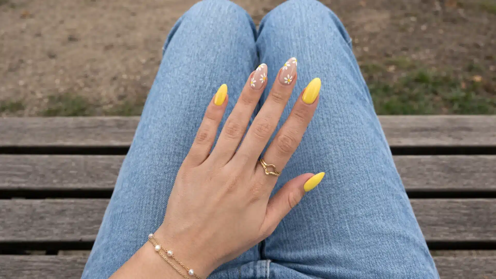 Hand with butter yellow wildflower field nails resting on jeans showing bright floral spring nails design