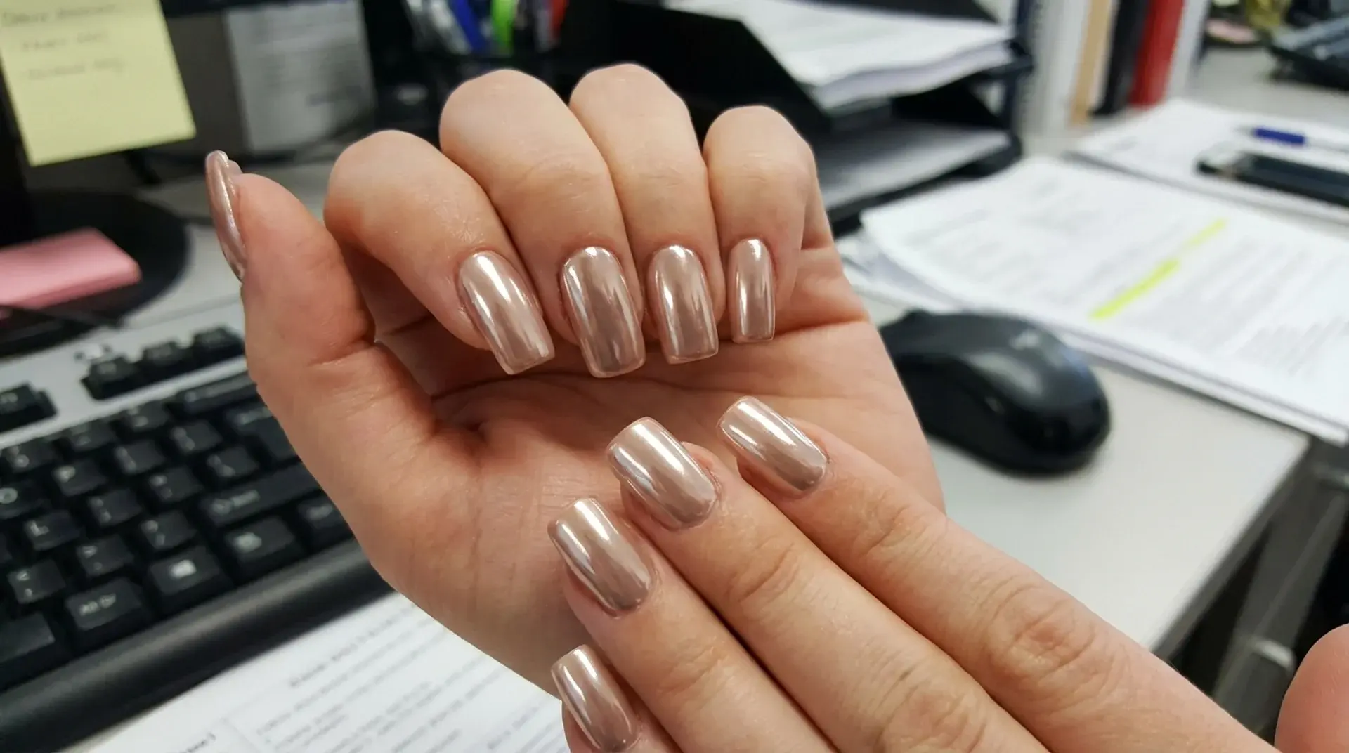 Metallic chrome silver manicure with reflective finish shown on hand at office workspace