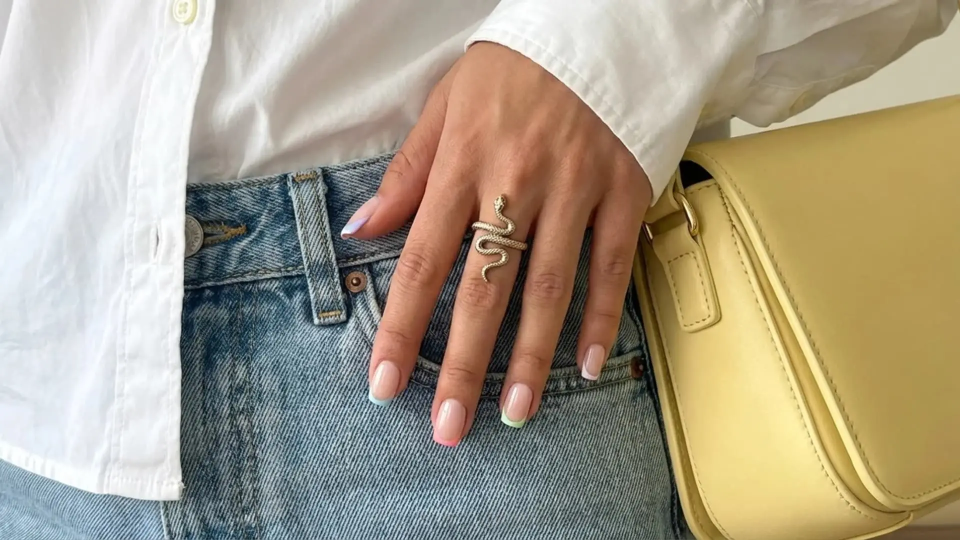 Natural manicure with pastel micro French tips holding yellow bag against denim outfit and white shirt as spring break nails idea
