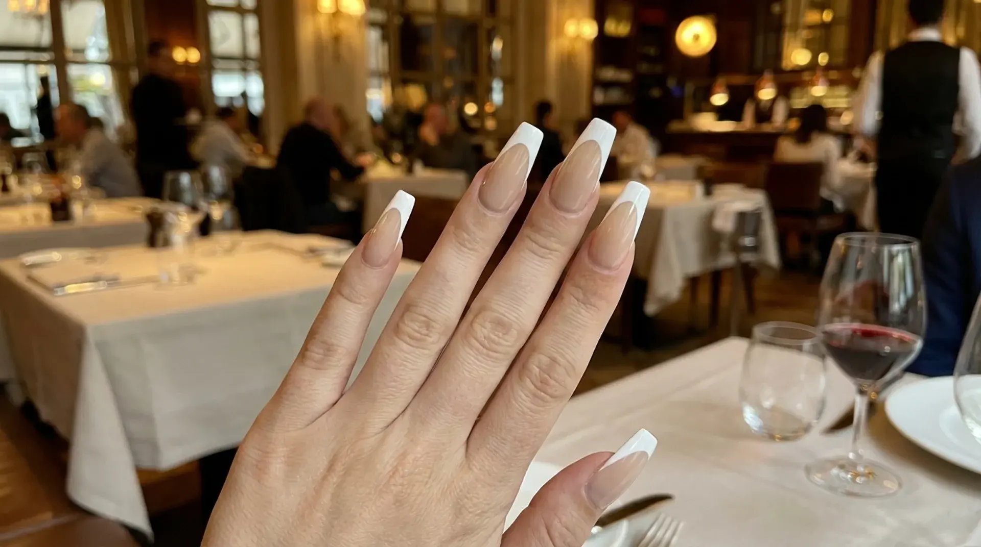 Neutral base French tip manicure shown in upscale restaurant dining setting