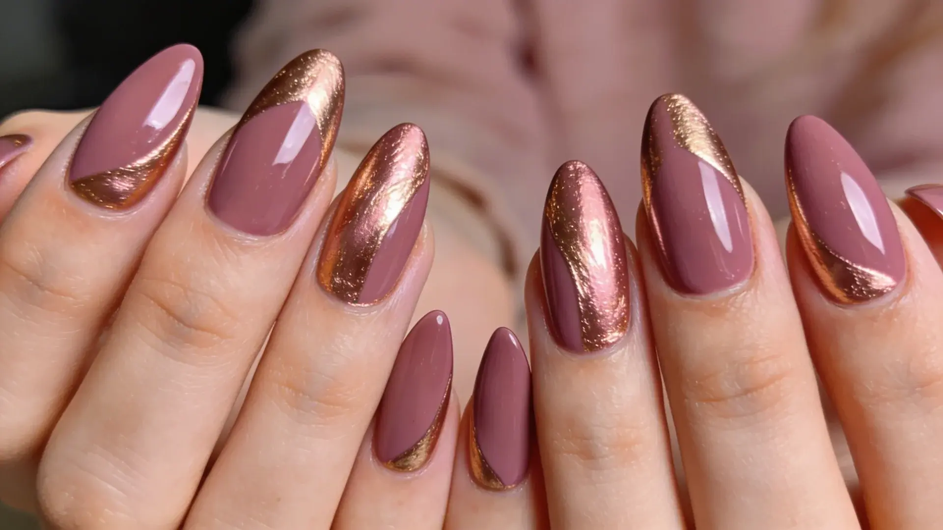 Rose gold accents placed over a mauve base create a warm color contrast on almond shape nails