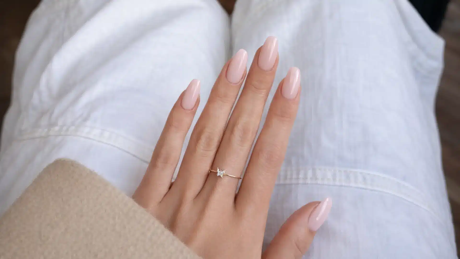 Soft glossy pink almond manicure on hand with ring displayed showing clean strawberry milk nails style