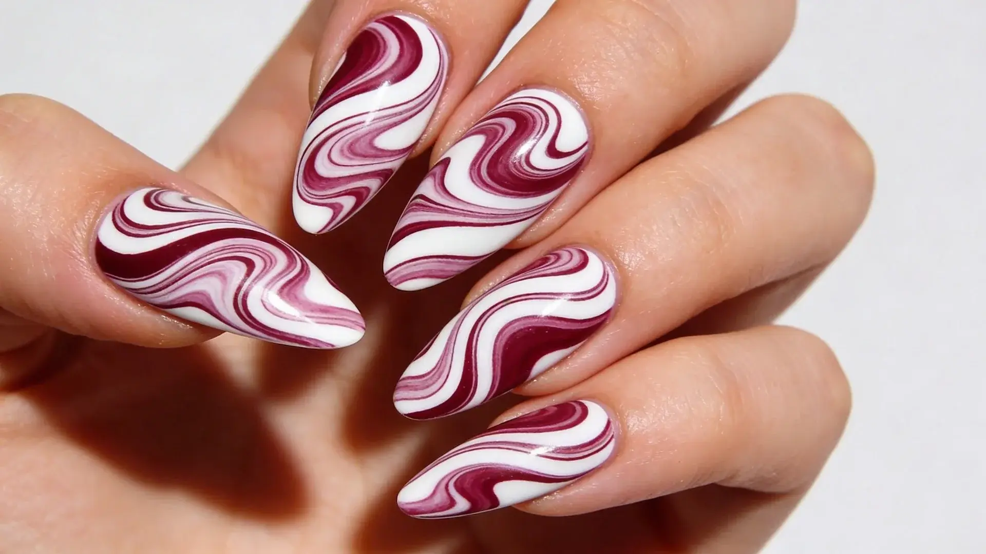 Soft swirling lines in white or deeper mauve shades create movement across the nails on a almond shape nials