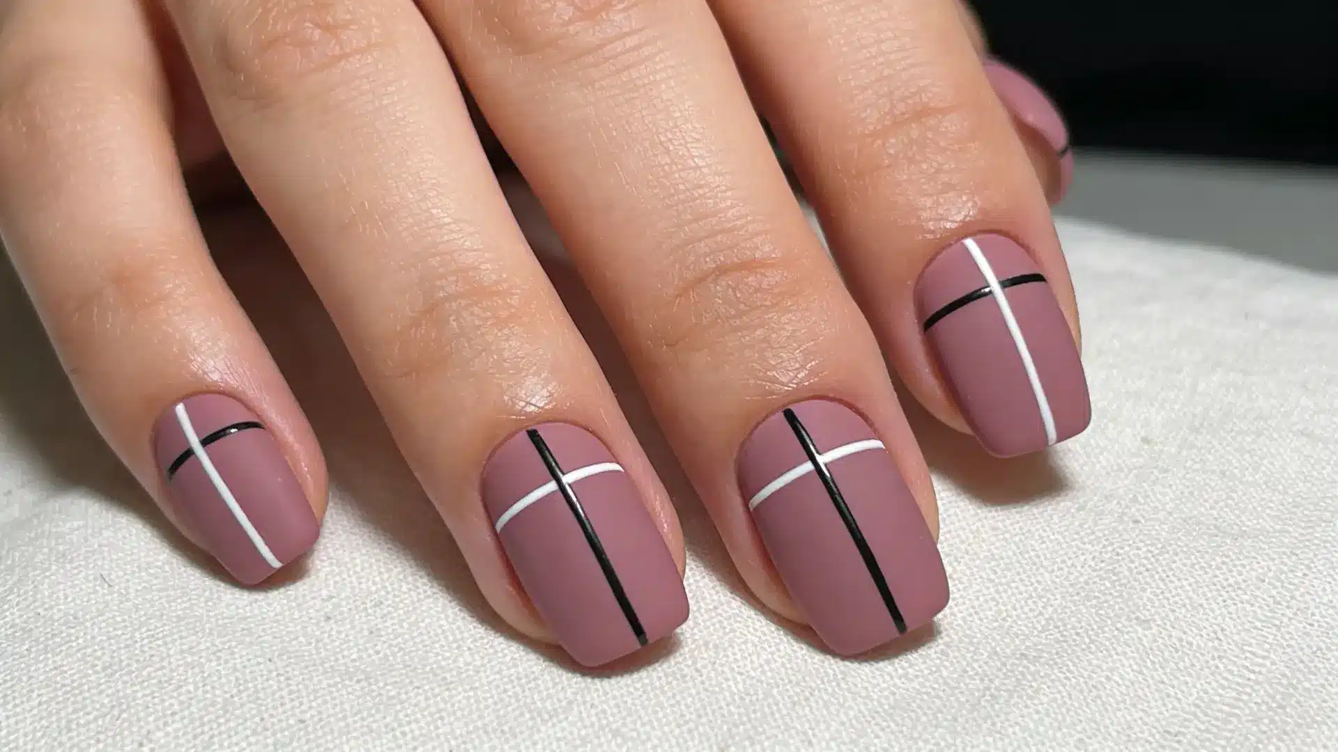Thin black or white lines drawn across a mauve base create a modern manicure on short square nails