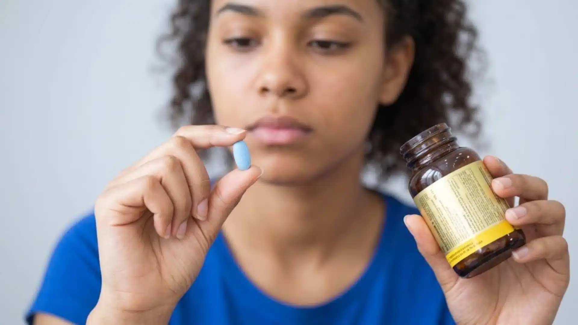 Woman holding a blue pill and medicine bottle, showing oral acne treatment and daily medication use