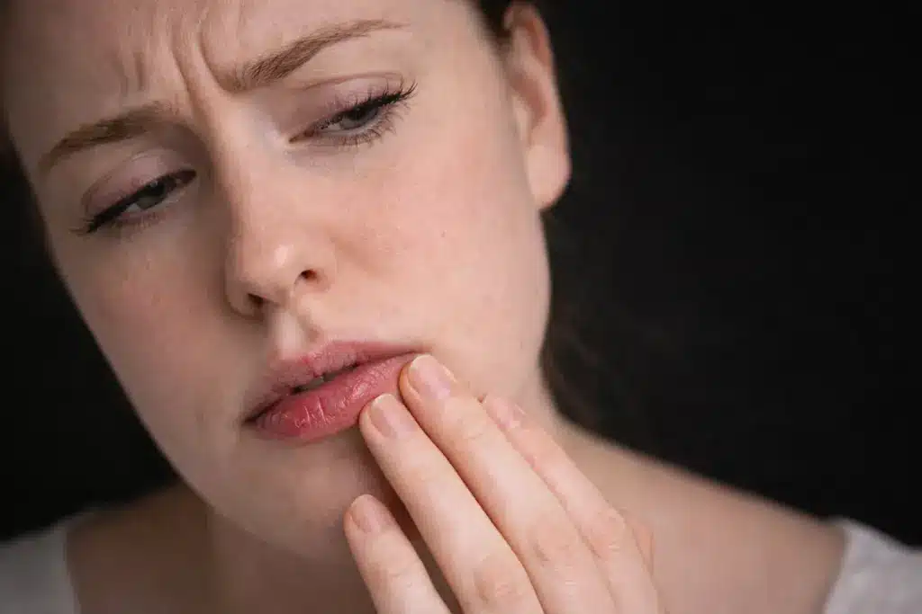 Woman touching irritated lips showing sensitivity and discomfort, highlighting potential risks of lip blush for certain skin types