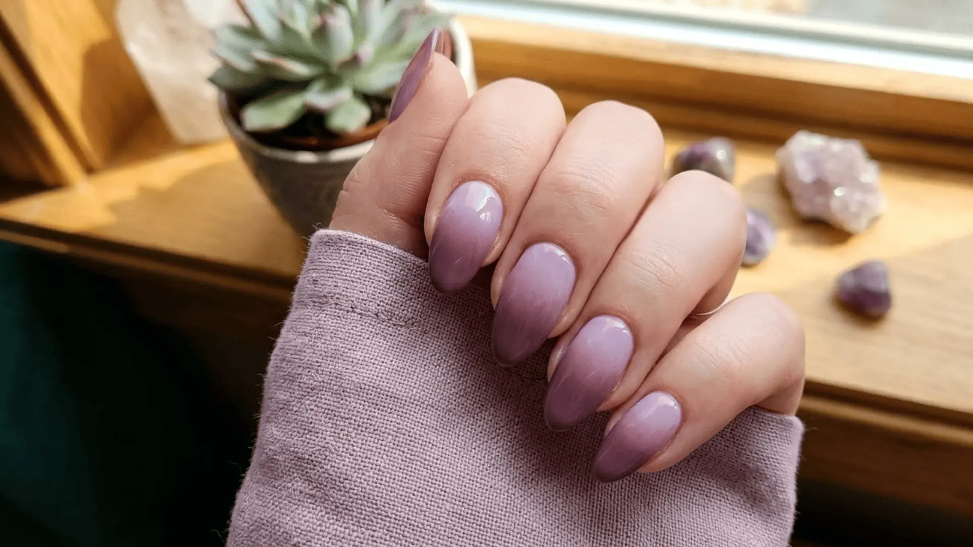 mauve ombre nails in an almond shape, held against a lavender sleeve