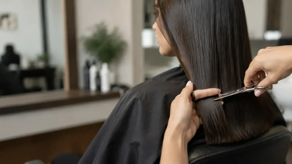 A hairstylist is trimming long hair in a salon with scissors and a comb during a haircut session