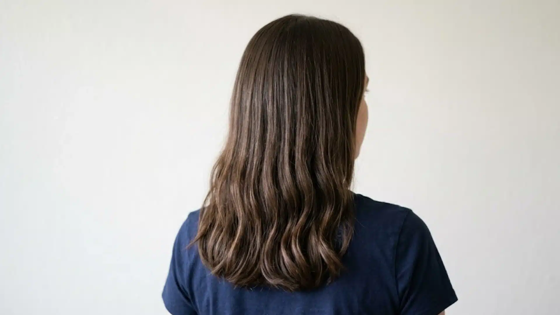 Back view of medium length dark brown 1C hair with soft natural waves and textured ends indoors