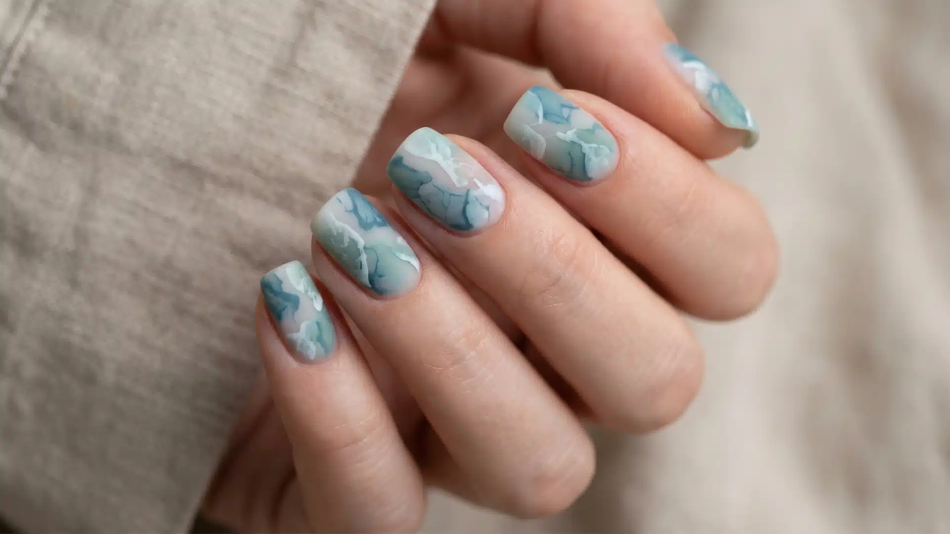 Close-up of matte blue and white marble nail art on short nails