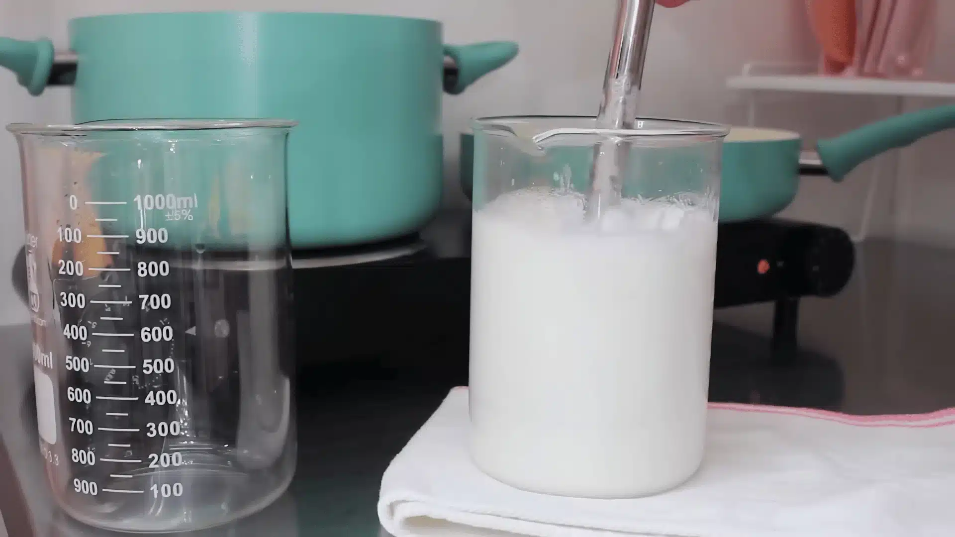 Freshly blended lotion mixture in a beaker with immersion blender on kitchen counter