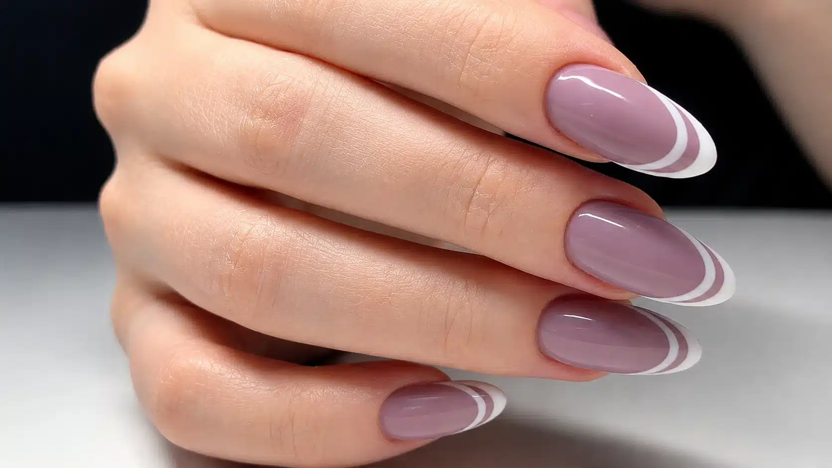 Glossy almond-shaped nails with soft mauve polish and elegant white French tips in close-up macro view.