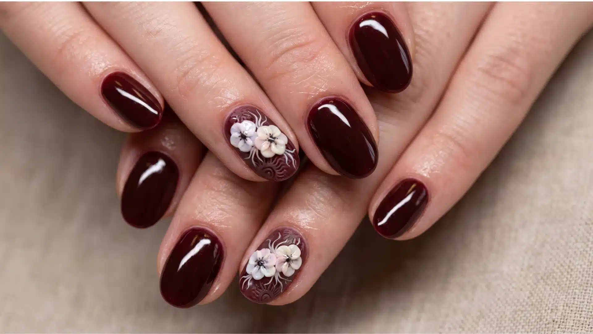 Glossy burgundy nails with small white floral accents on two fingers