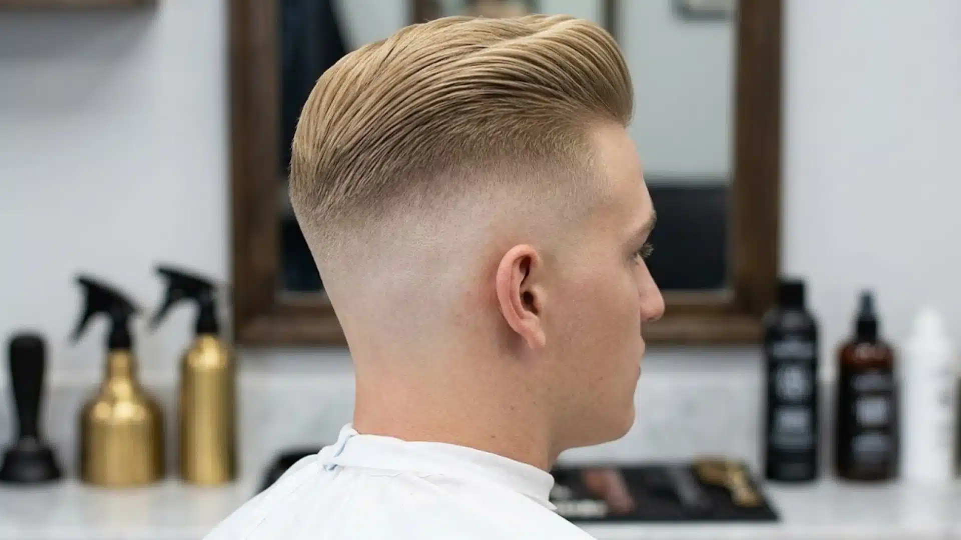 High skin fade haircut with slicked back blond hair and clean shaved sides in a modern barbershop