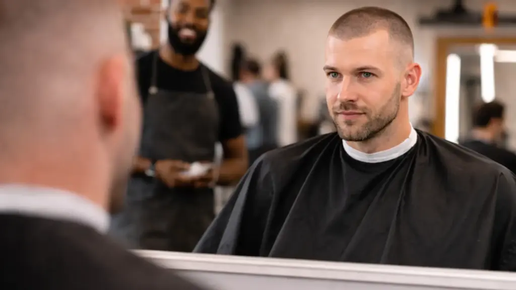 Man with fresh buzz cut haircut sitting in barber chair with cape showing close cropped sides and uniform length