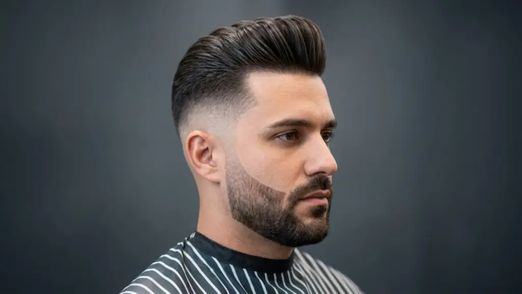 Man with sharp mid skin fade haircut and styled pompadour sitting against a plain background