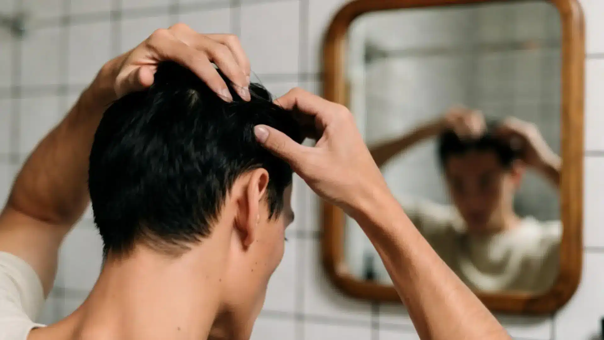 Person examining a mole on the scalp in a bathroom mirror for skin health concerns