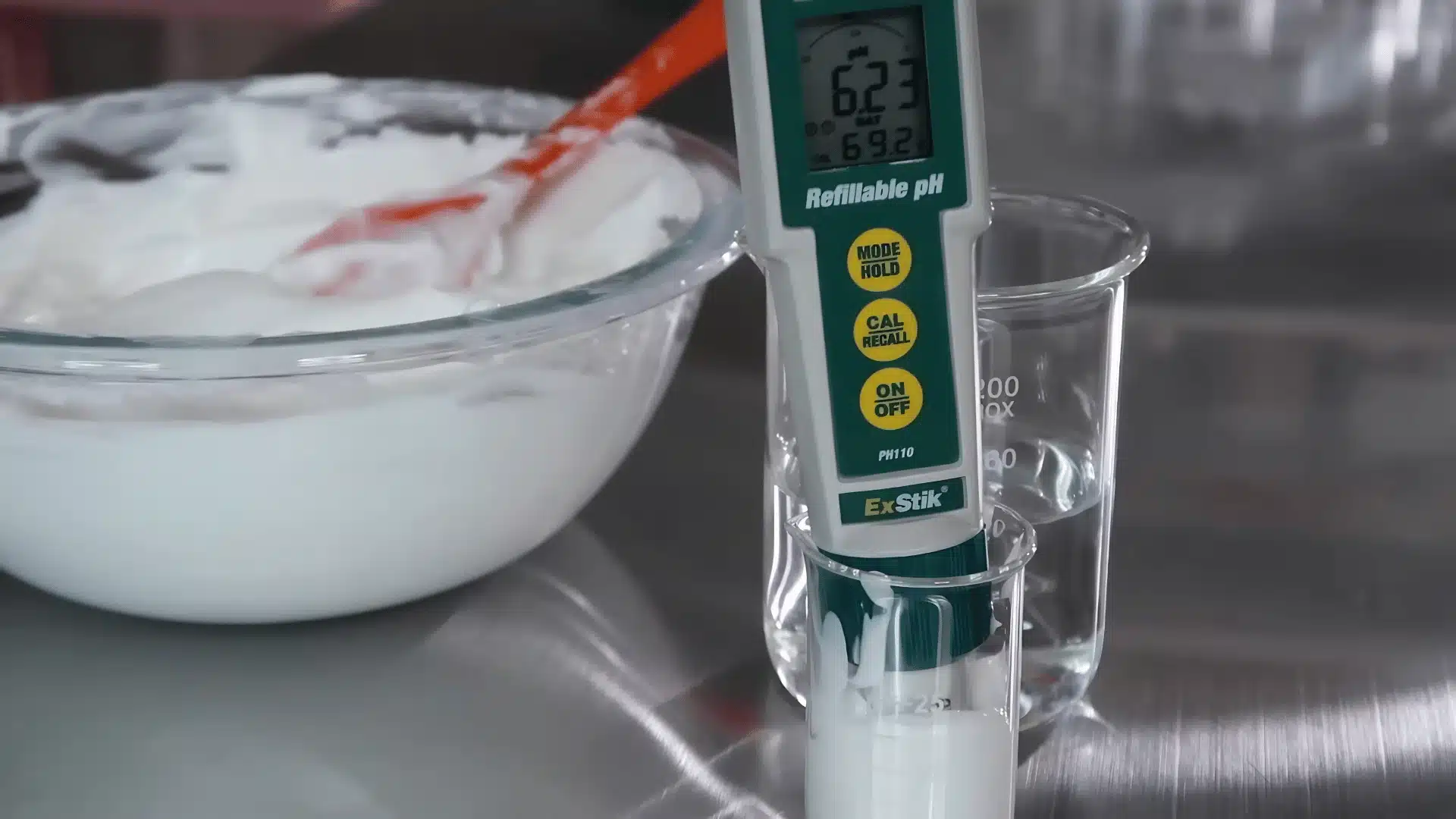 pH meter testing homemade lotion mixture in a glass container on a steel surface