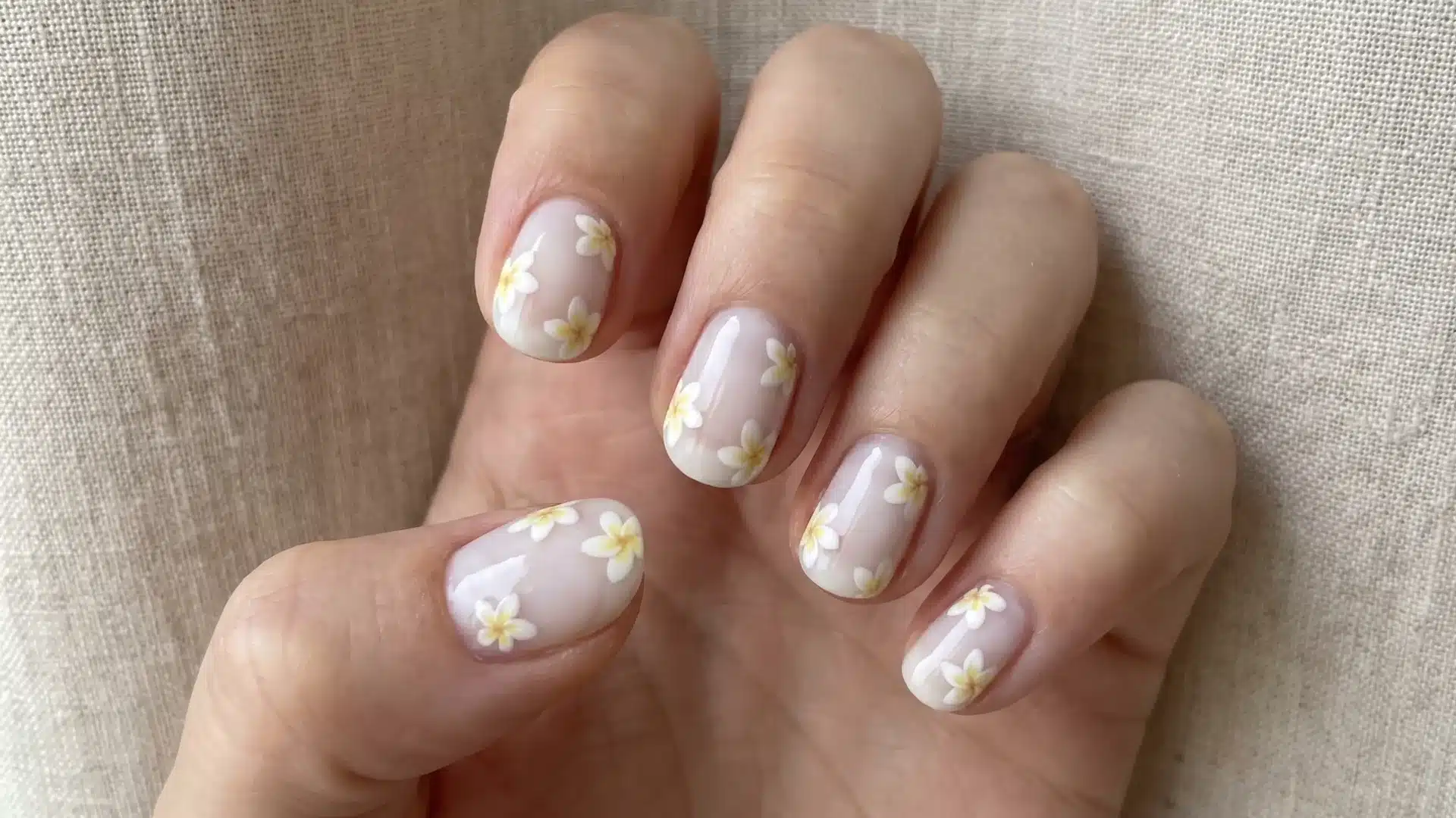 Sheer blush nails with scattered white frangipani flowers and soft yellow centers