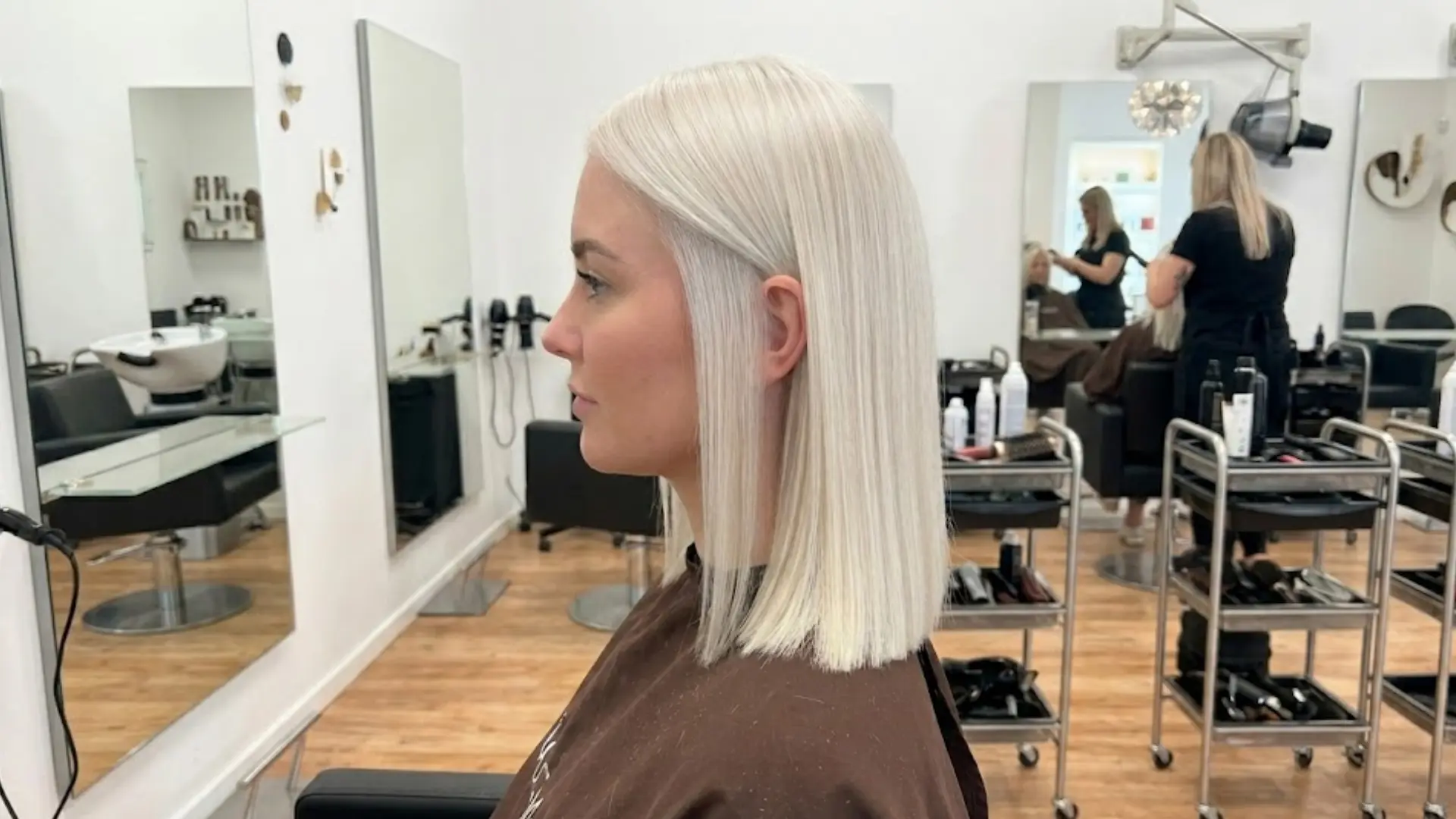 Side profile of woman with sleek platinum blonde straight hair in salon chair with mirrors behind