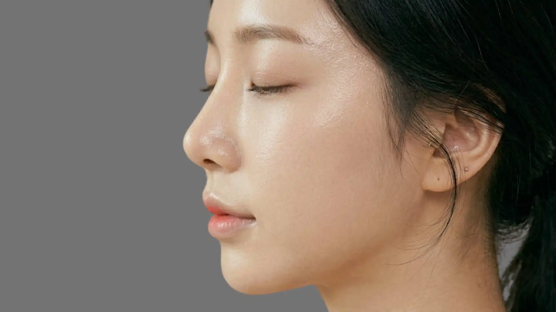 Side profile of woman with smooth glowing skin, straight nose, soft features, and natural makeup reflecting Korean beauty standards