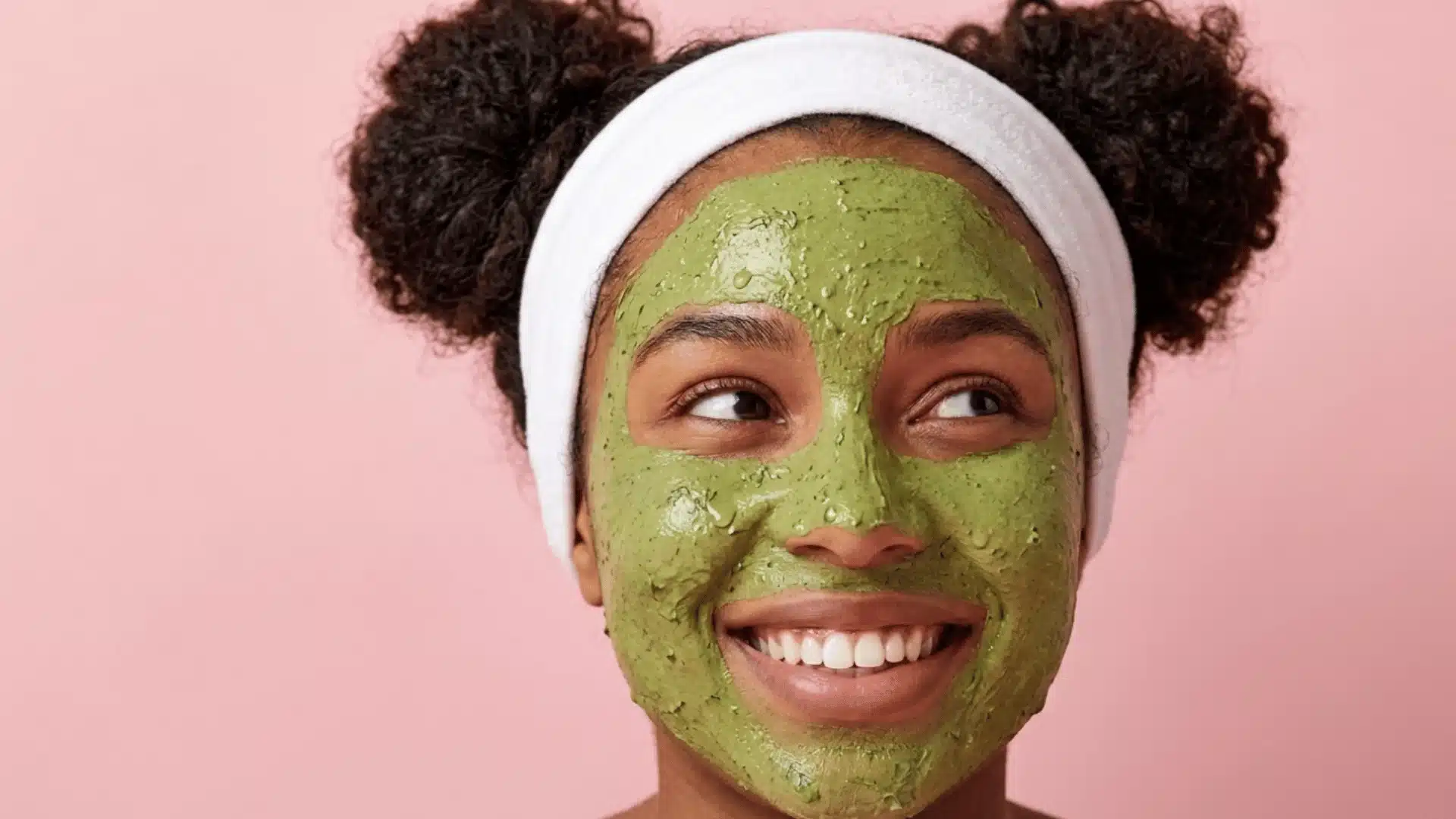 Smiling woman wearing a lemon balm face mask with a white headband against a soft pink background