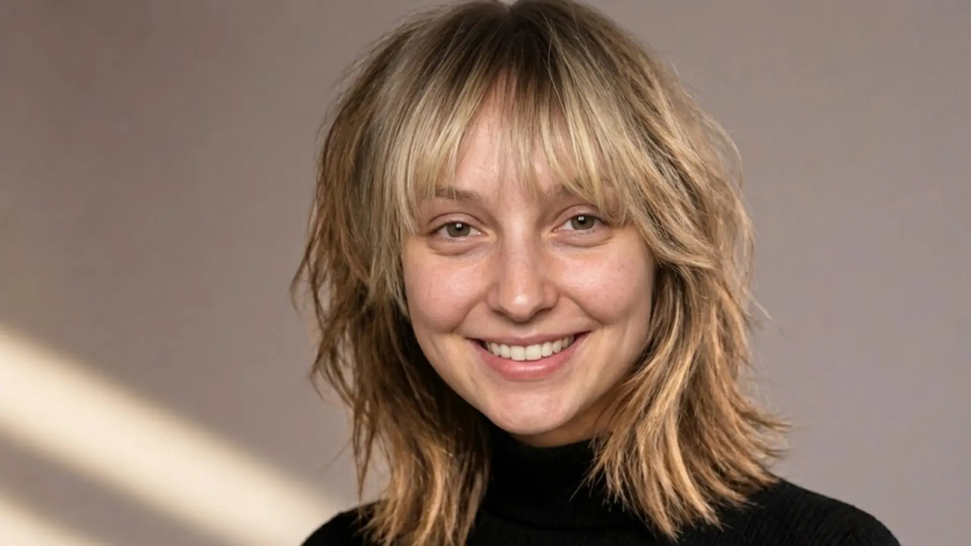Smiling woman with shaggy shoulder length blonde hair and soft bangs, natural texture and relaxed casual look