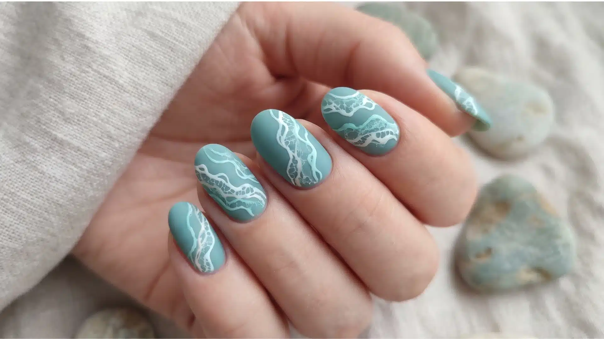 Teal matte nails with delicate white seafoam pattern on a soft hand