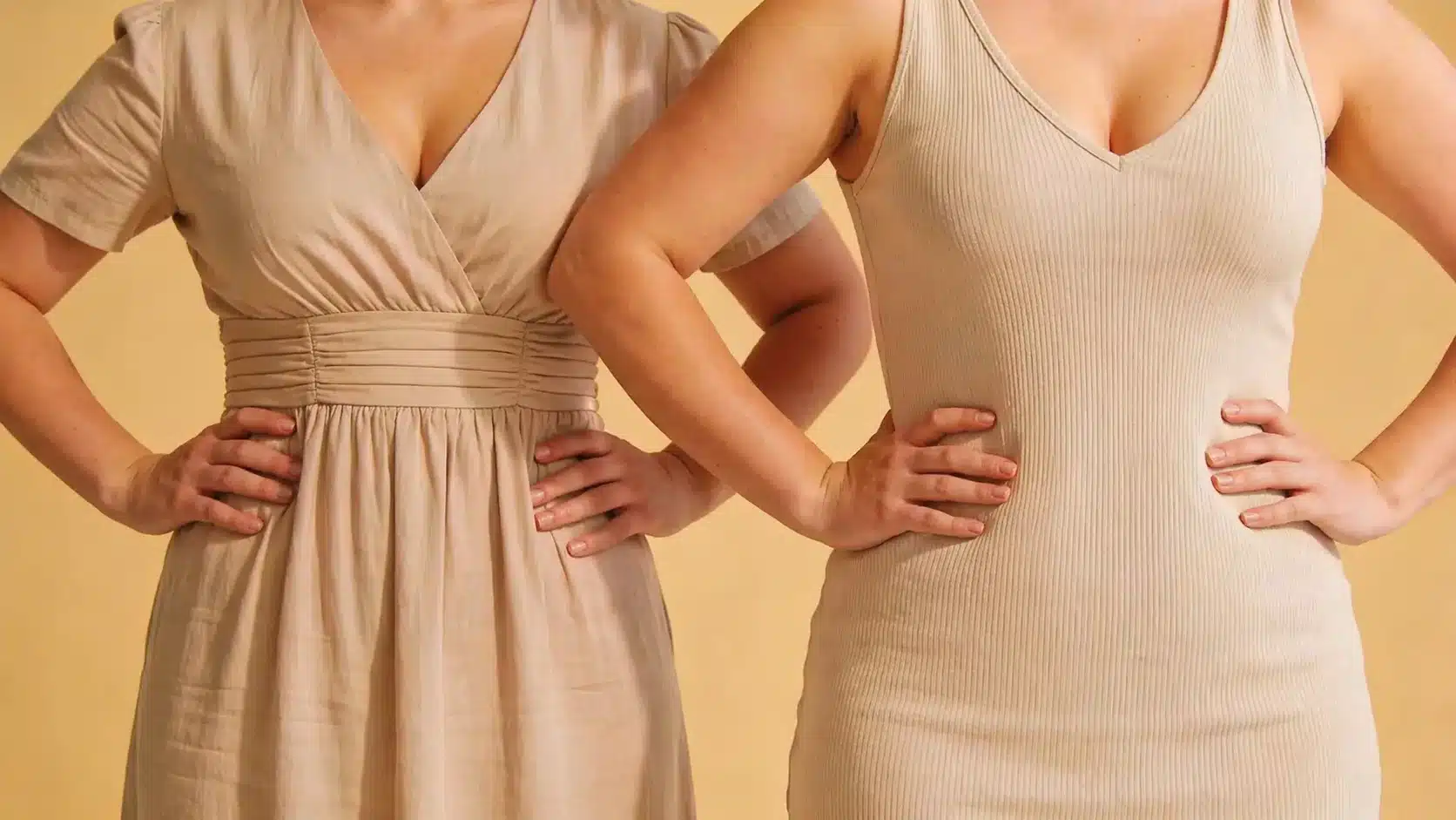 Two women in beige dresses with hands on waist against a clean neutral studio background
