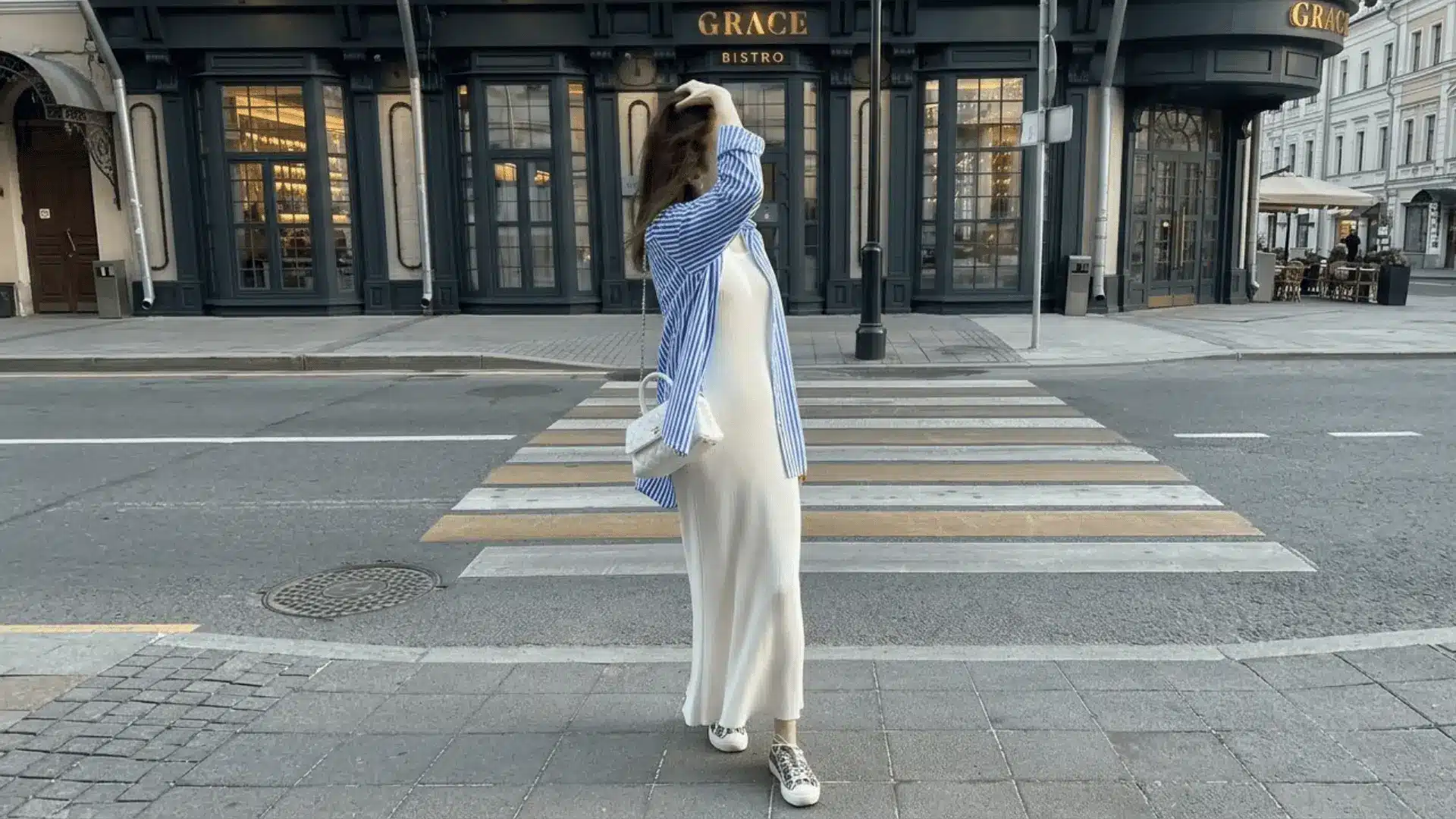Woman in white midi dress layered with blue striped shirt walking on street casual chic outfit idea