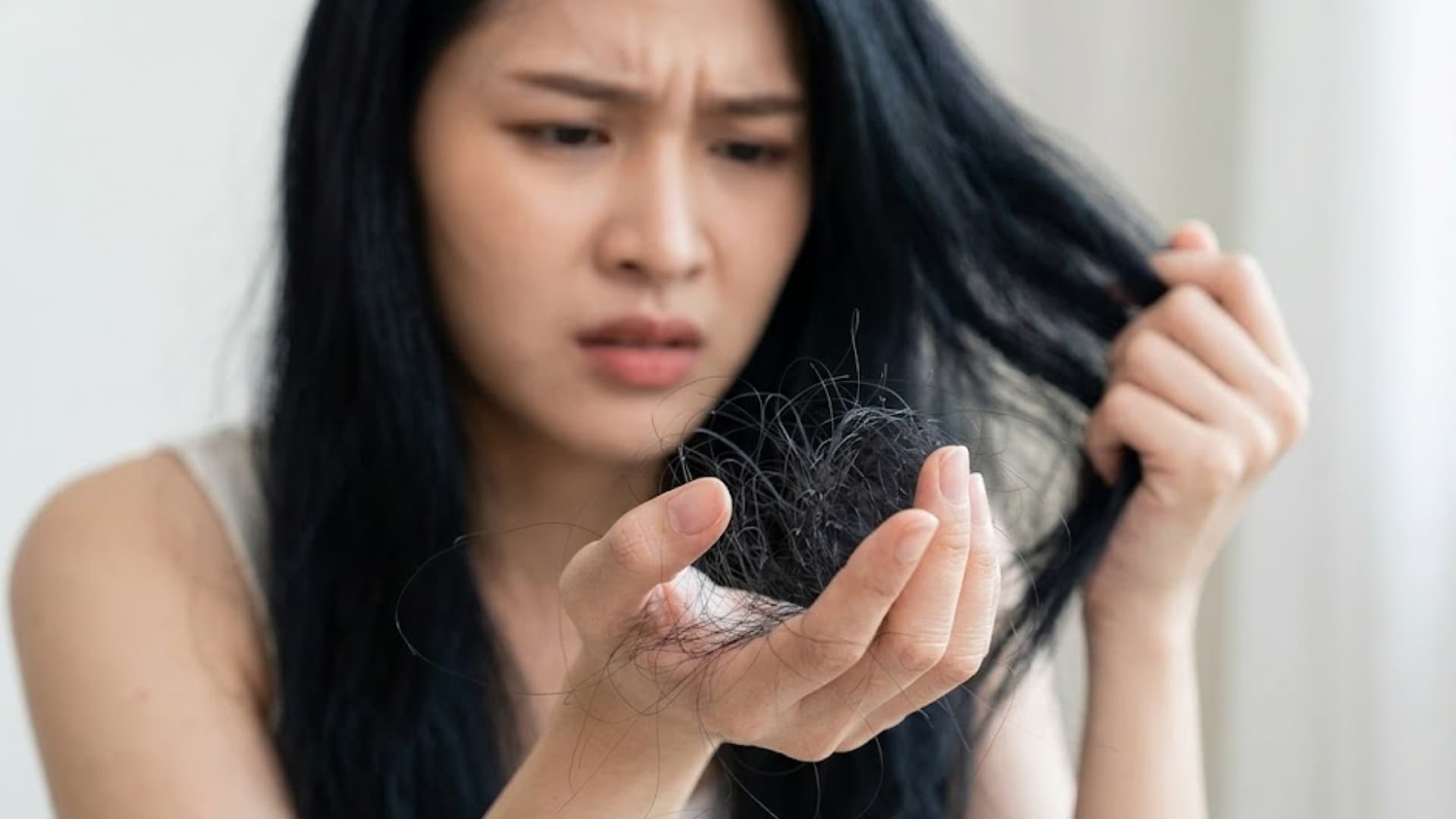 Woman looking concerned while holding hair strands in hand, showing noticeable hair shedding and possible hair loss issue