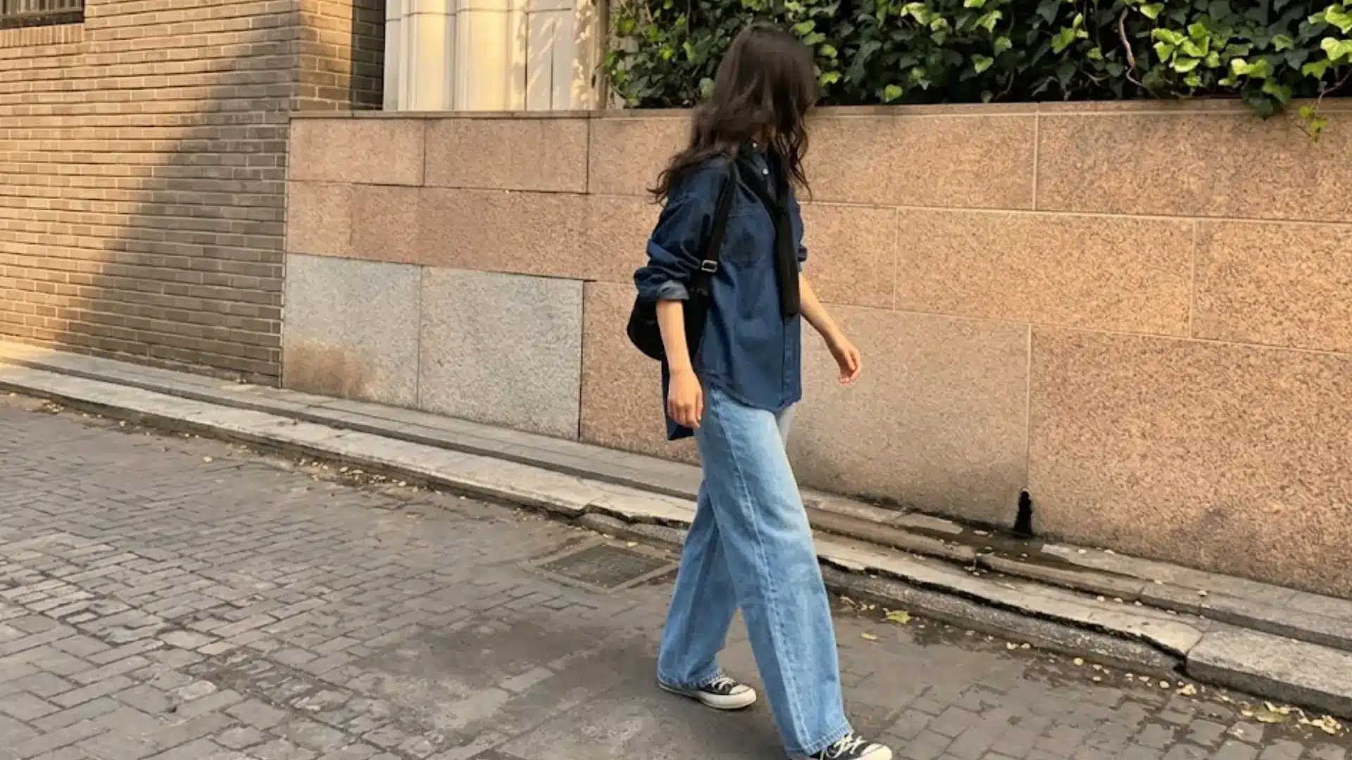 Woman walking in loose blue jeans and dark shirt with sneakers minimal street style casual outfit