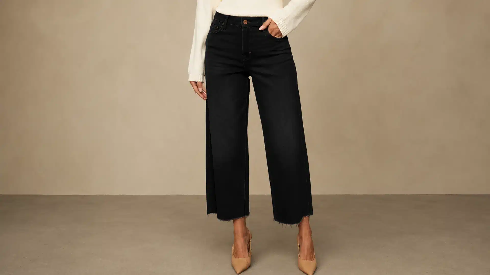 A cropped view of a person wearing black wide-leg crop jeans, a white sweater, and nude heels