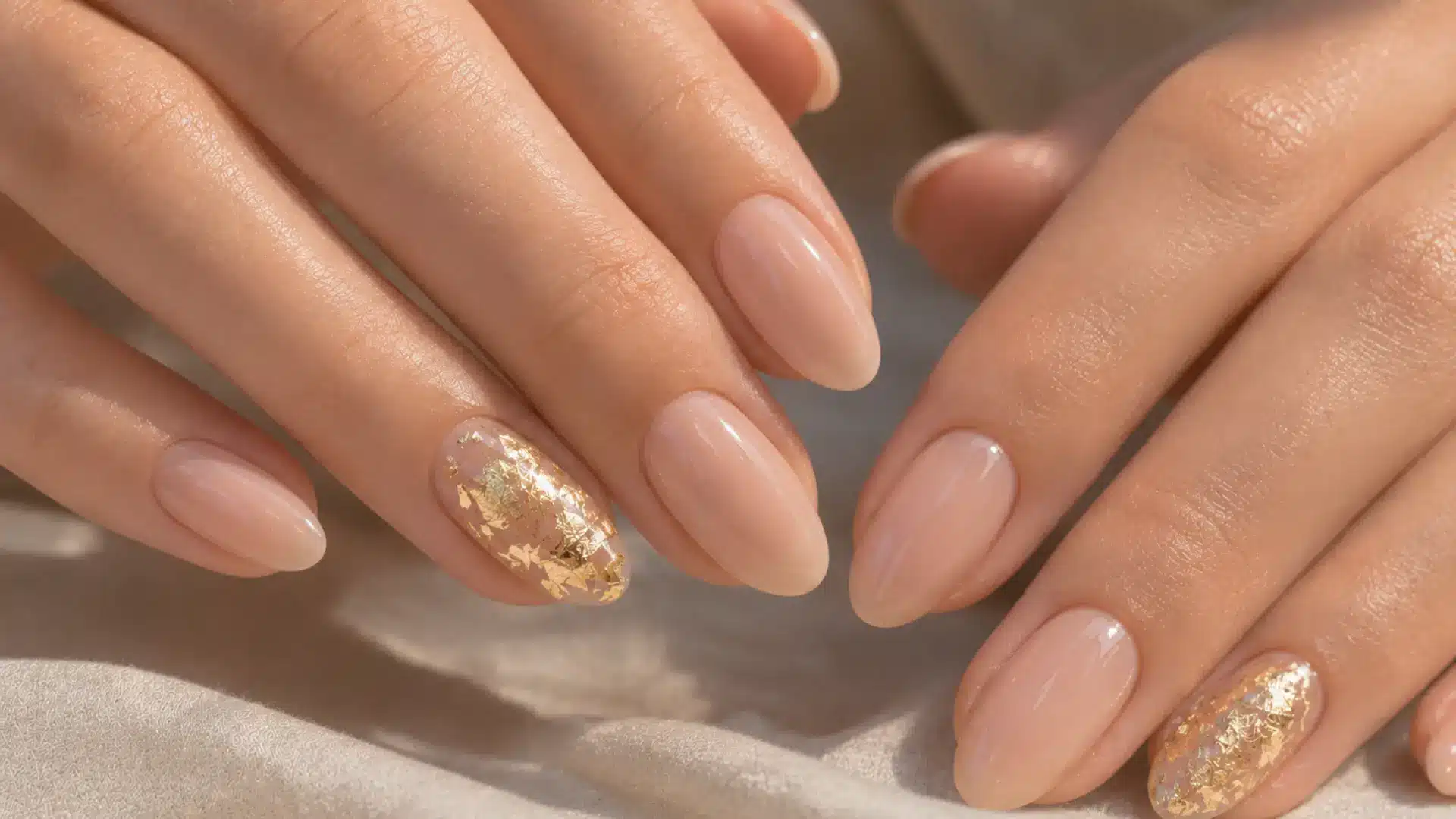 Almond nails with gold leaf foil accent nail on sheer nude base, catching warm light