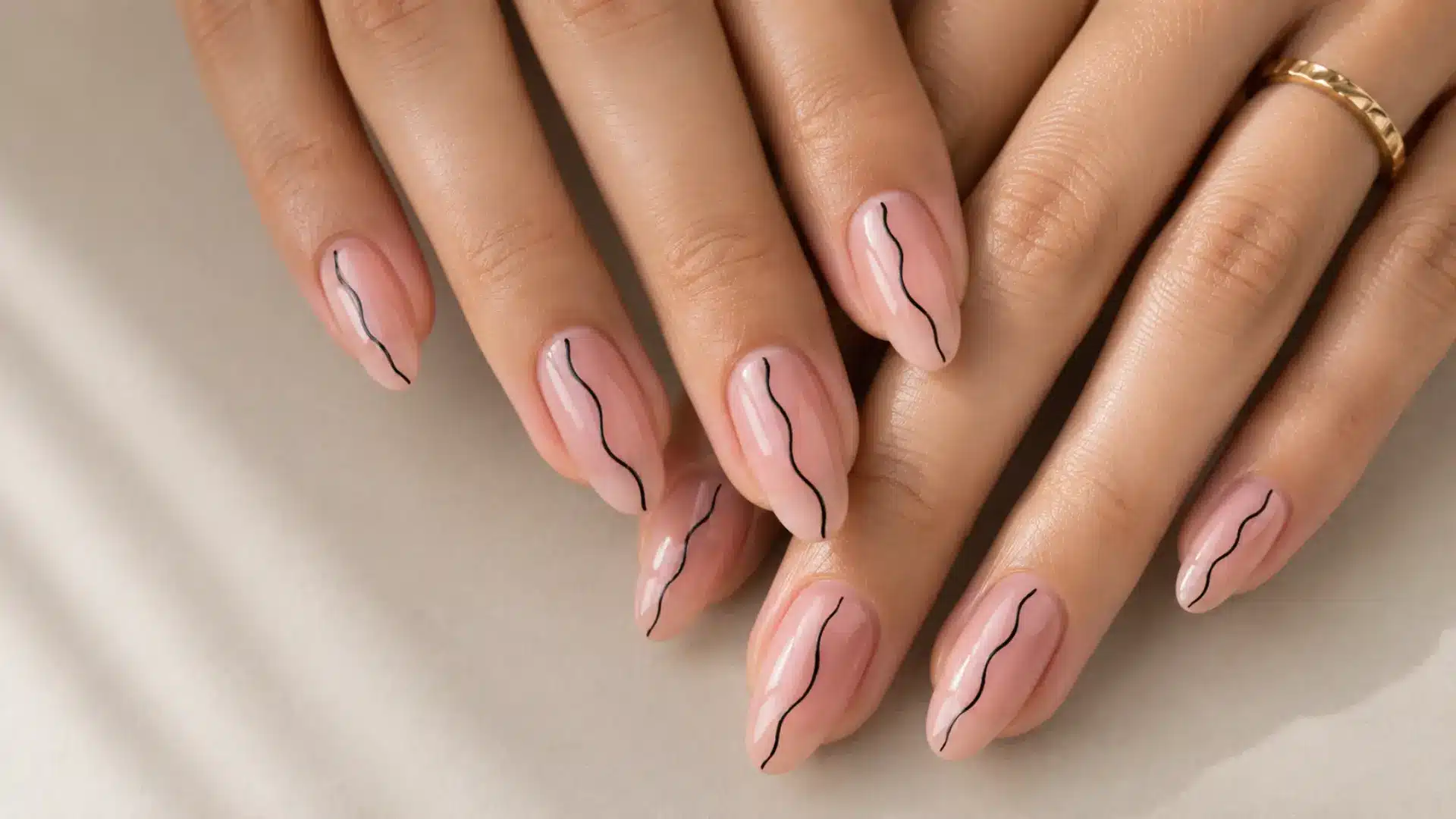 Almond nails with a single freehand black wavy line on a sheer pink glossy base