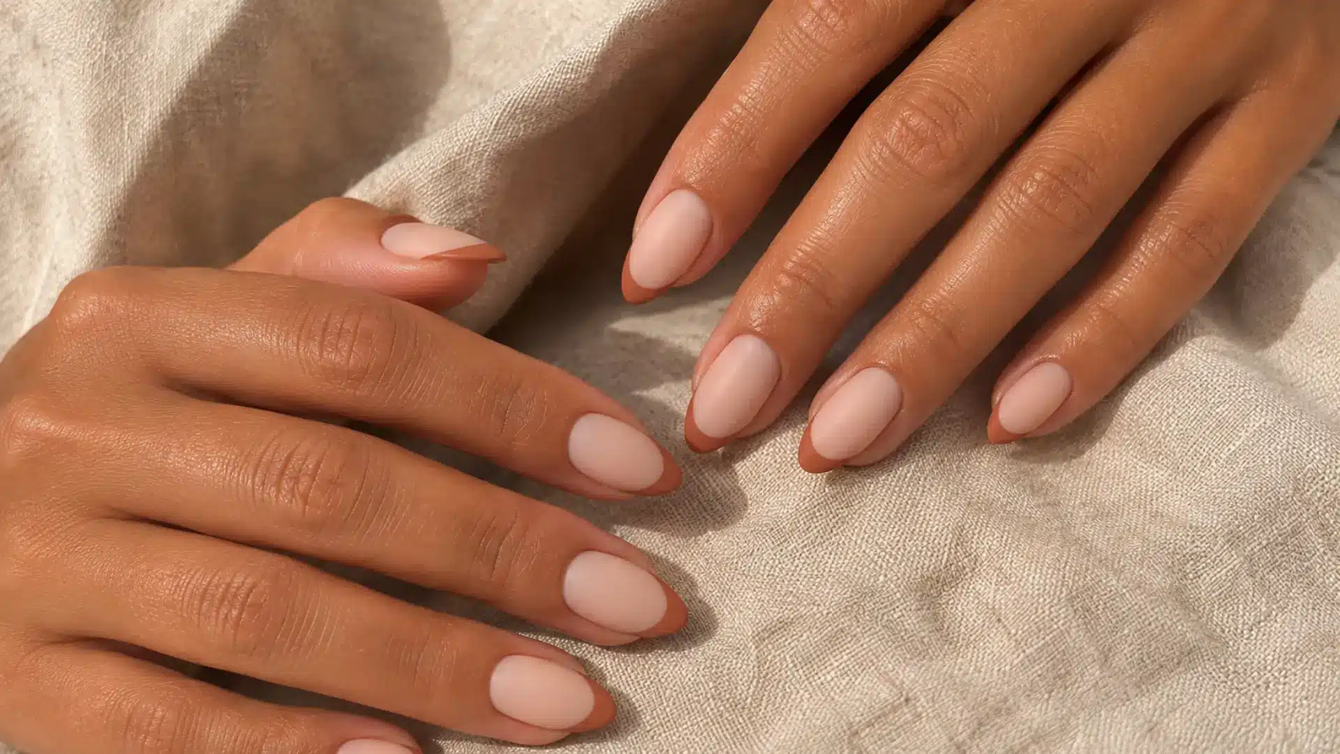 Almond nails with a terracotta matte French tip on a sheer nude base, editorial style