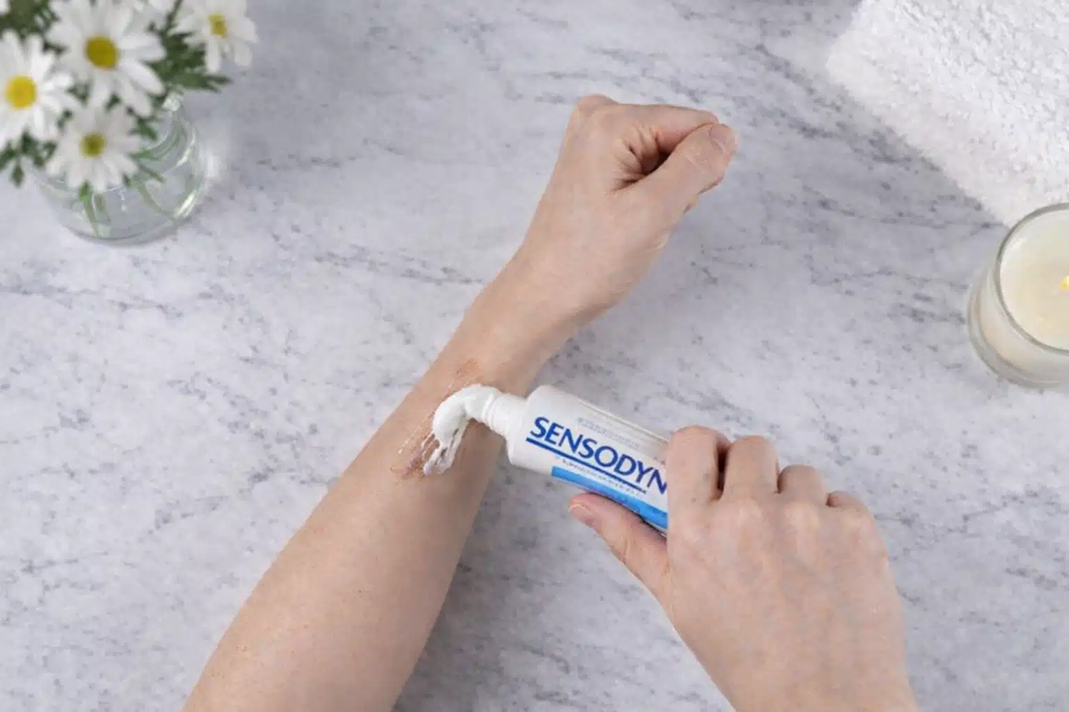 Applying non-gel toothpaste on forearm to remove hair dye stains, shown on marble surface with soft lighting setup