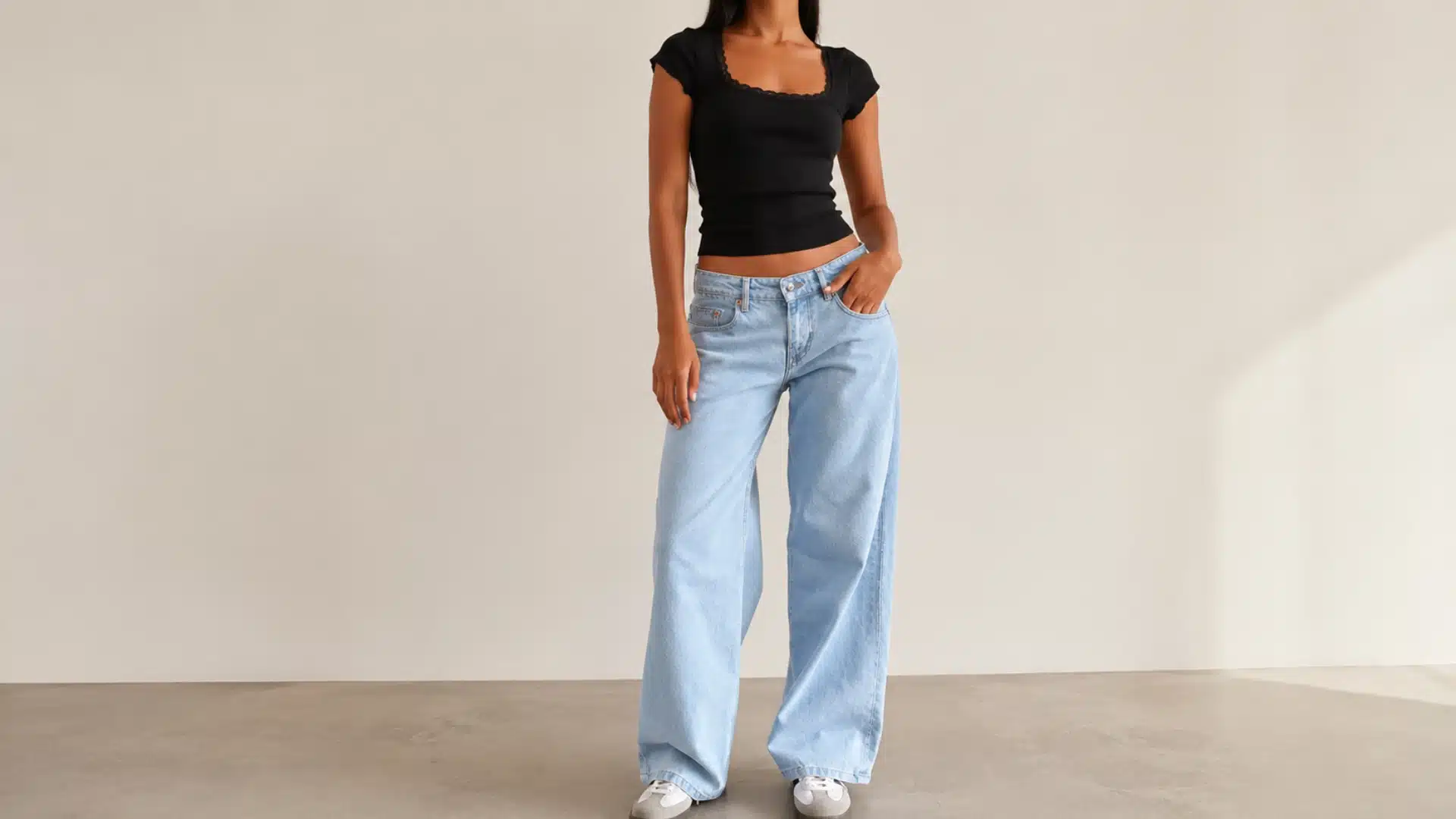 A woman wears a black short-sleeved top and light-wash, wide-leg jeans against a neutral background.