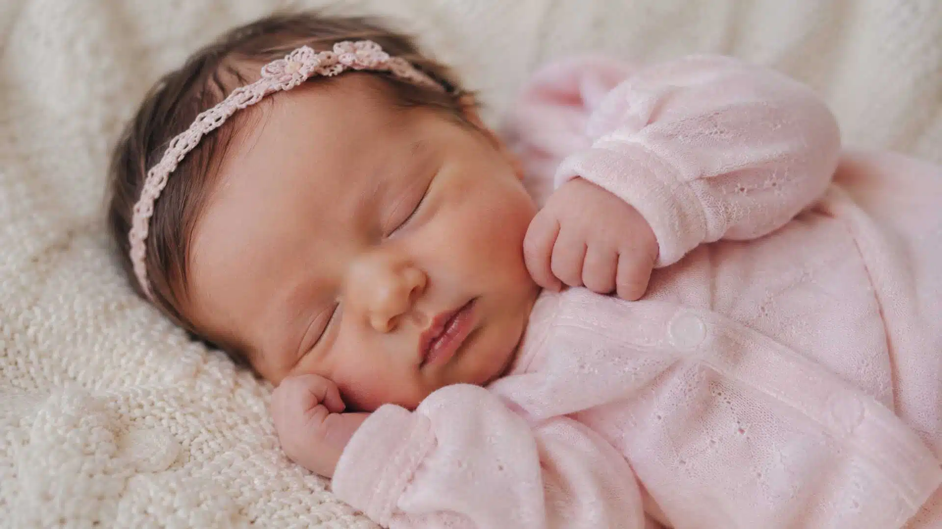 Baby girl in blush pink footed sleeper with crochet headband for newborn photoshoot