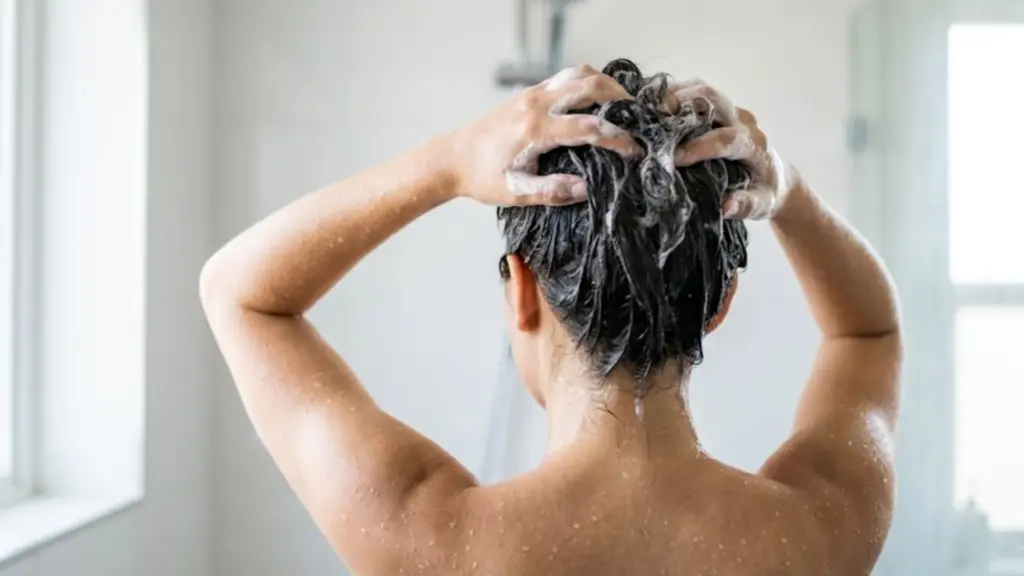 Back view of a person washing their hair with soapy lather in a bright shower