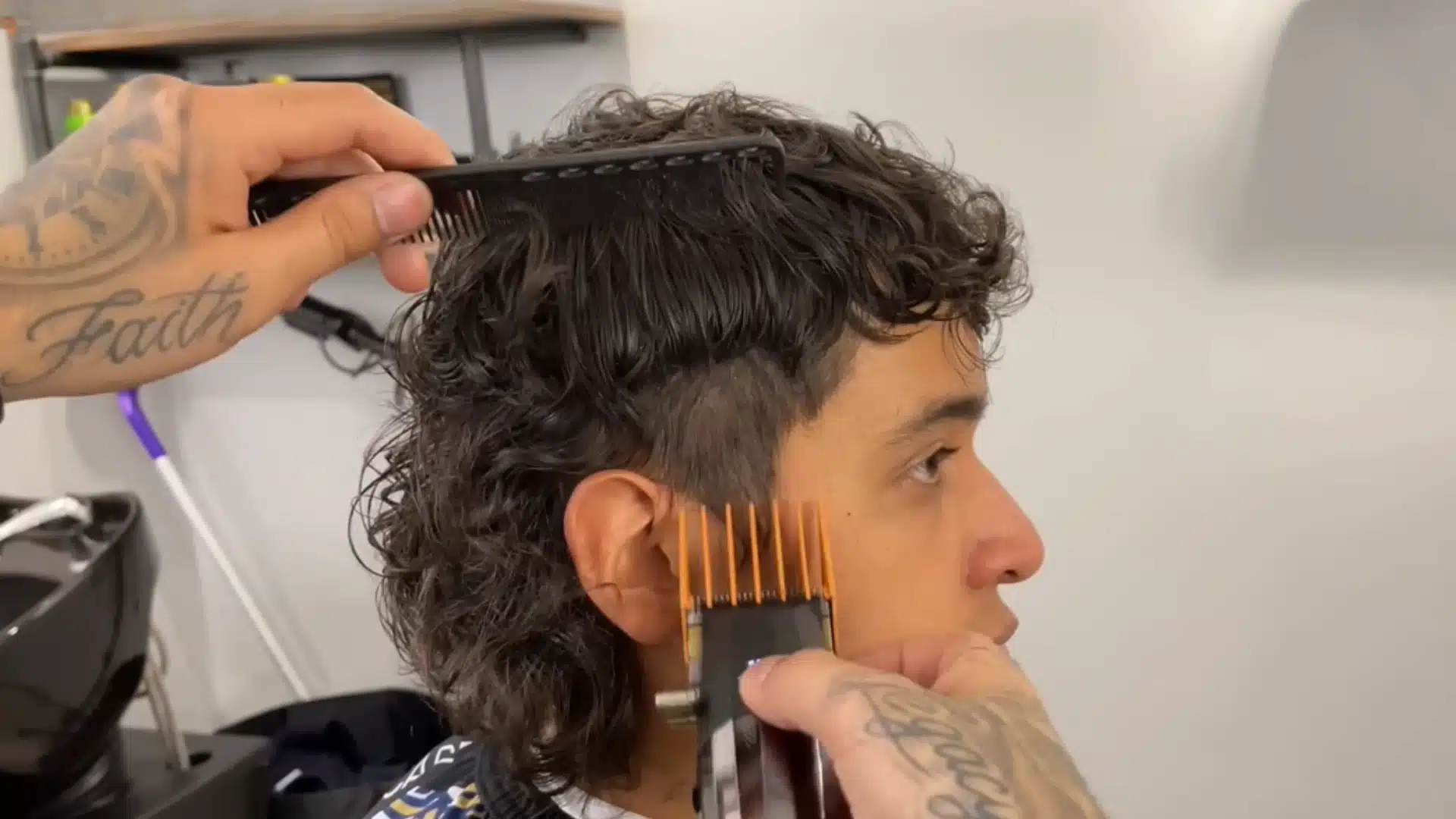 Barber blends a taper fade on curly hair with clippers and comb for a clean, sharp side finish