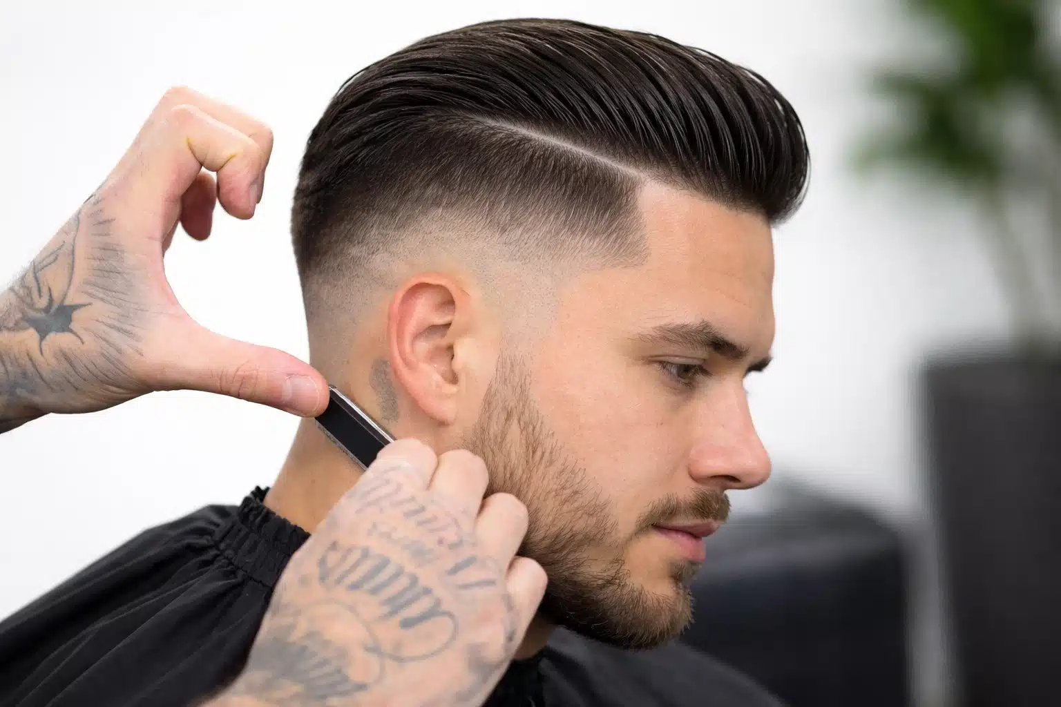 Barber shaping a high fade slick back haircut with razor part, detailing clean fade around ear and neckline