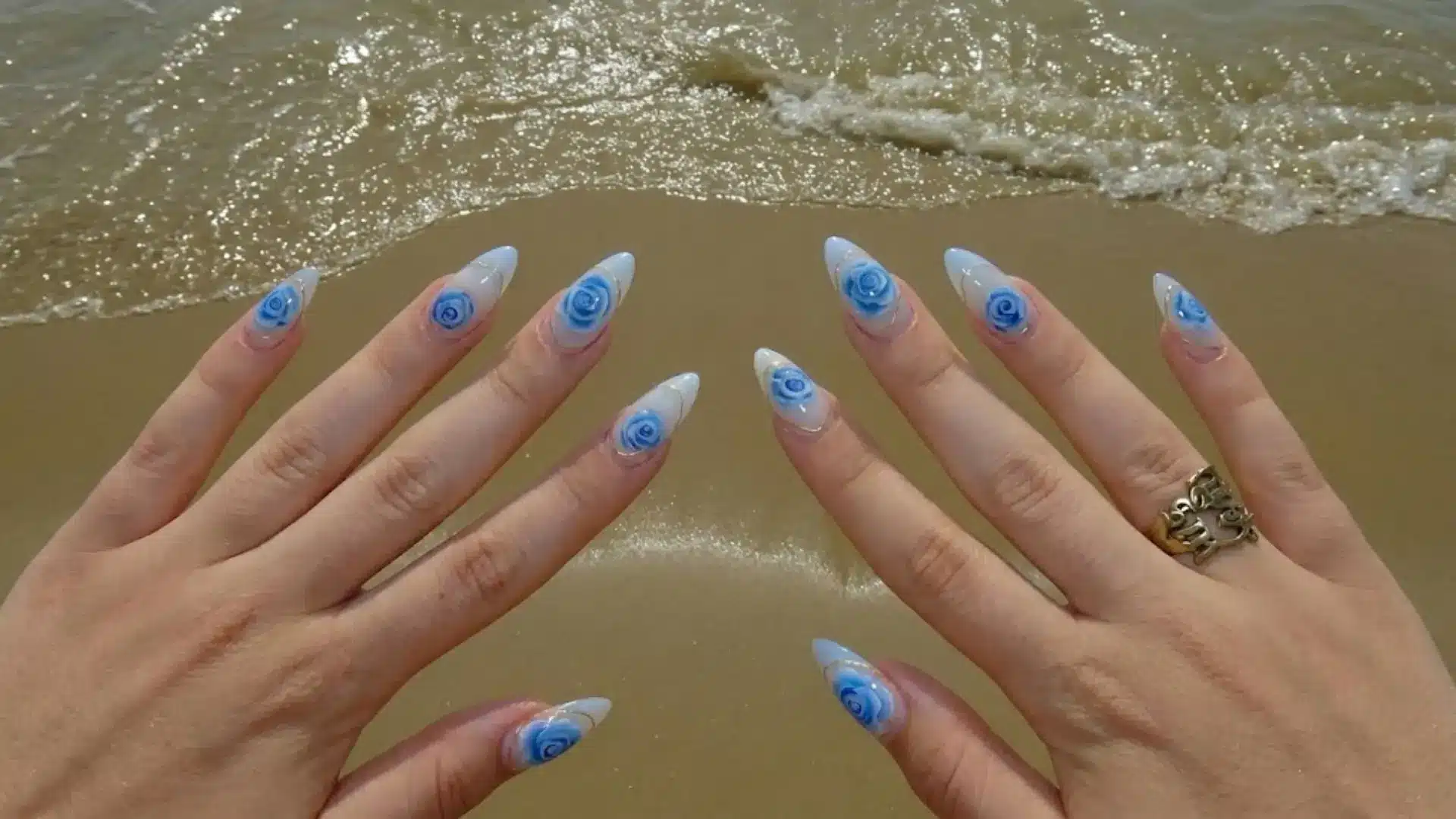 Blue rose acrylic nails over sandy beach background, glossy floral nail design for vacation manicure ideas