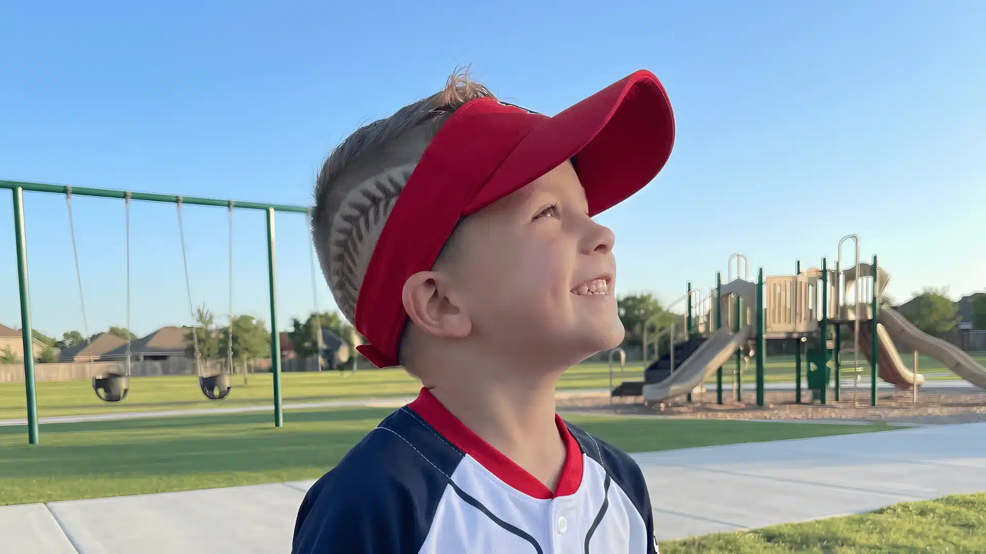 Boy in red visor smiling at sunny park playground