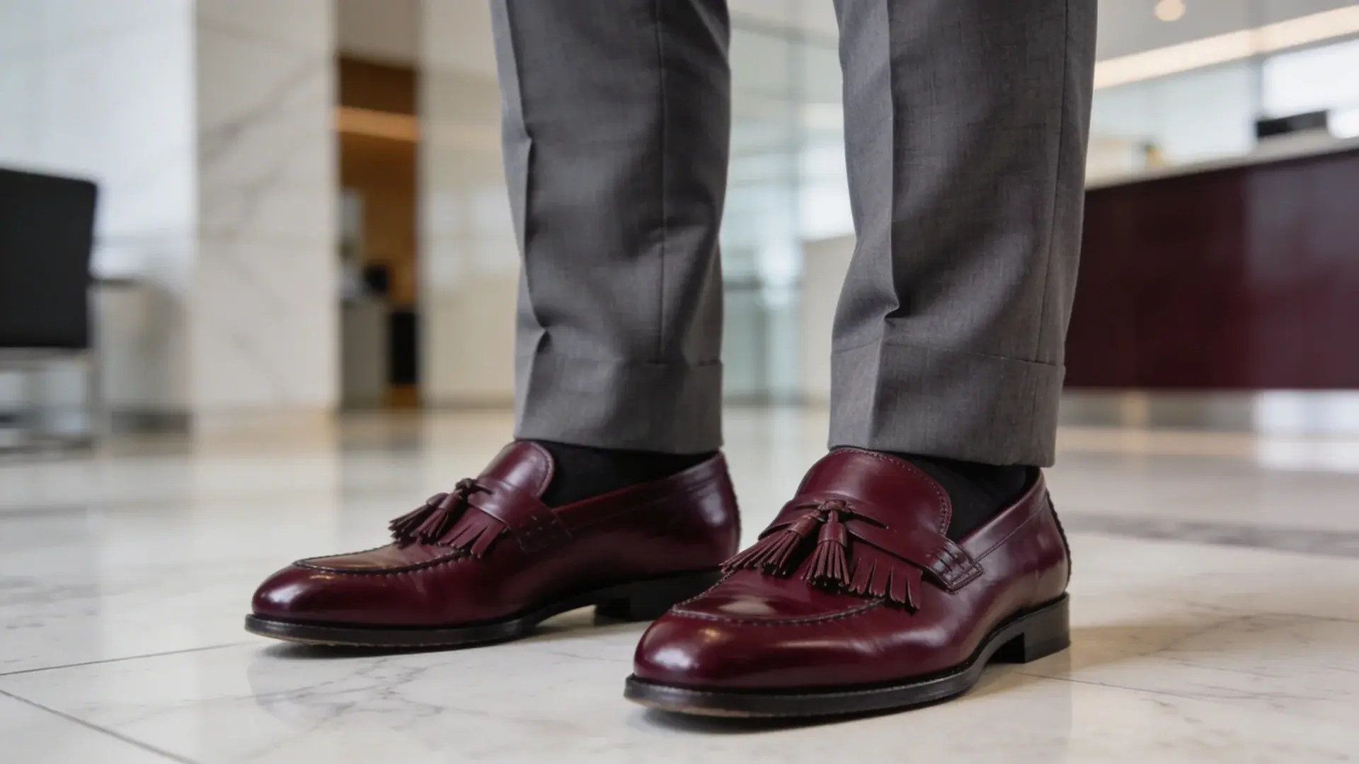 Burgundy kiltie loafers with grey trousers in office setting classic fringe detail formal mens footwear style